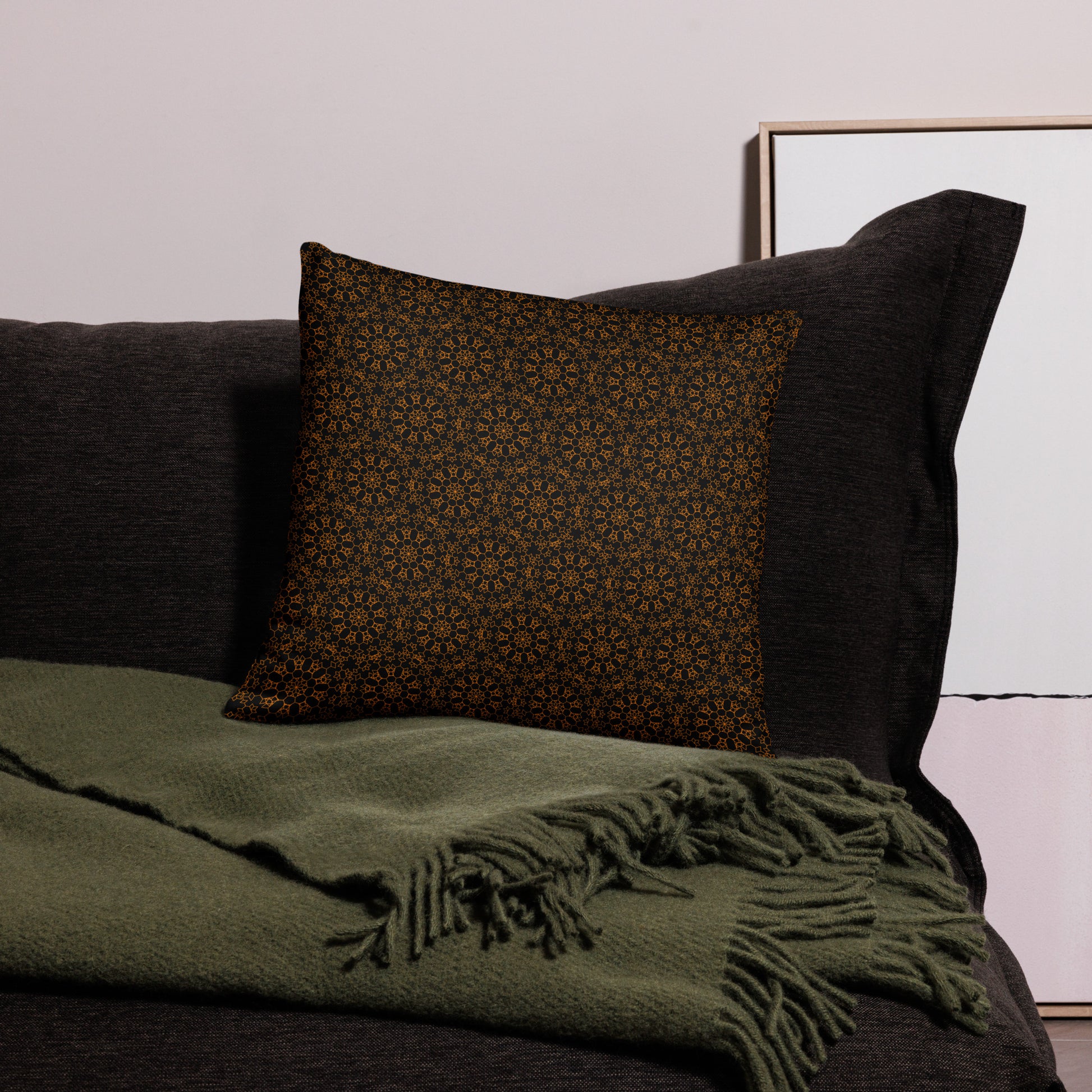 18″×18″ throw pillow with the 'Enneagon' black & gold geometric pattern on a dark sofa with green throw blanket.