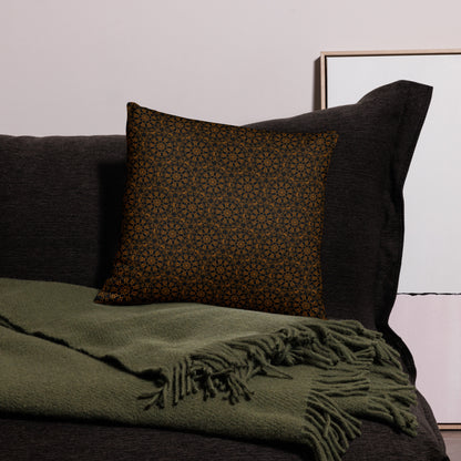 18″×18″ throw pillow with the 'Enneagon' black & gold geometric pattern on a dark sofa with green throw blanket.