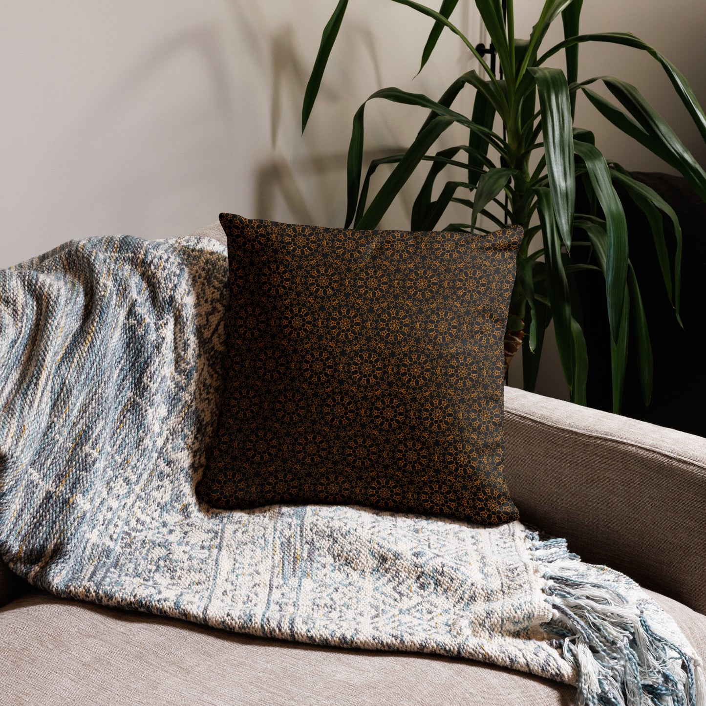 18″×18″ throw pillow with the 'Enneagon' black & gold geometric pattern on a sofa with textured throw blanket.