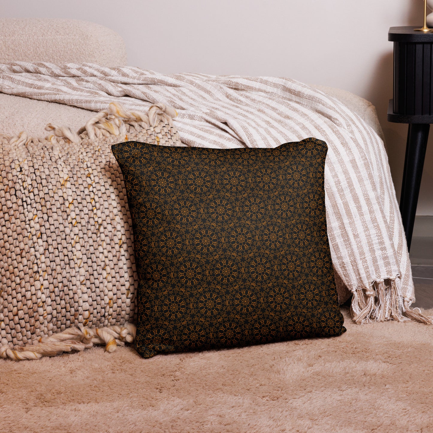 18″×18″ throw pillow with the 'Enneagon' black & gold geometric pattern on a bed with striped blanket.