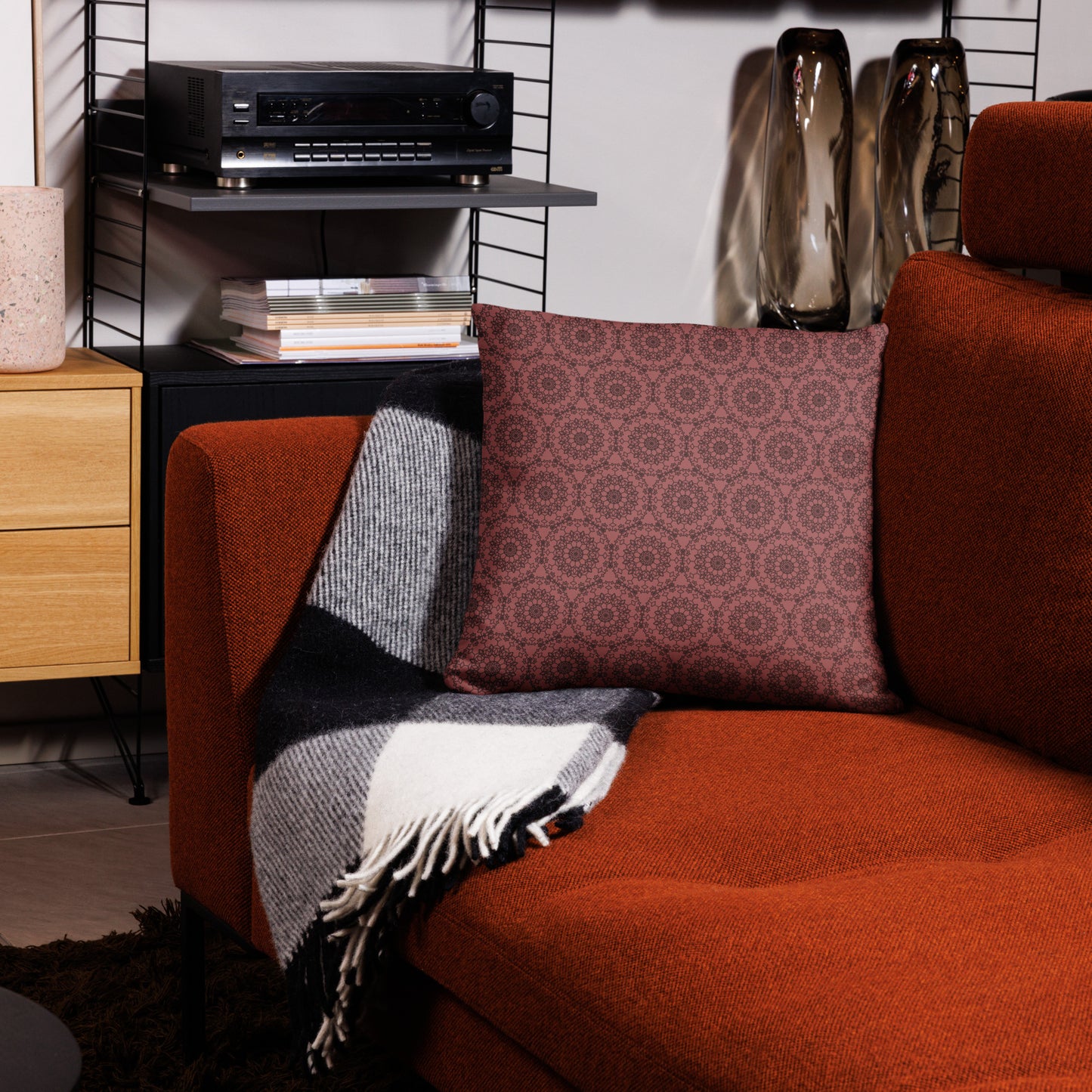 18″×18″ throw pillow with the 'Dodecagon' rose geometric pattern on orange armchair with checkered blanket.