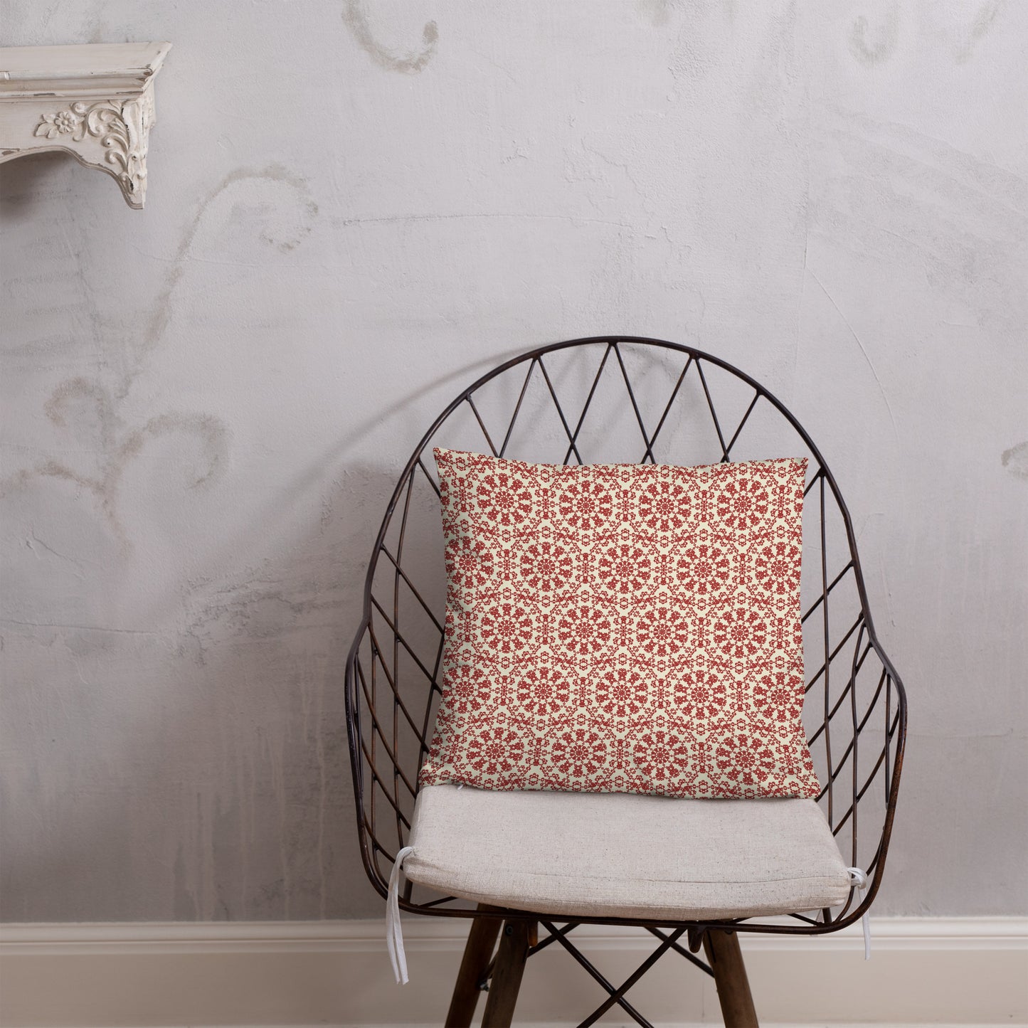 18″×18″ throw pillow with the ‘Decagon’ terracotta and beige geometric pattern on a wire chair against an ornate plaster wall.