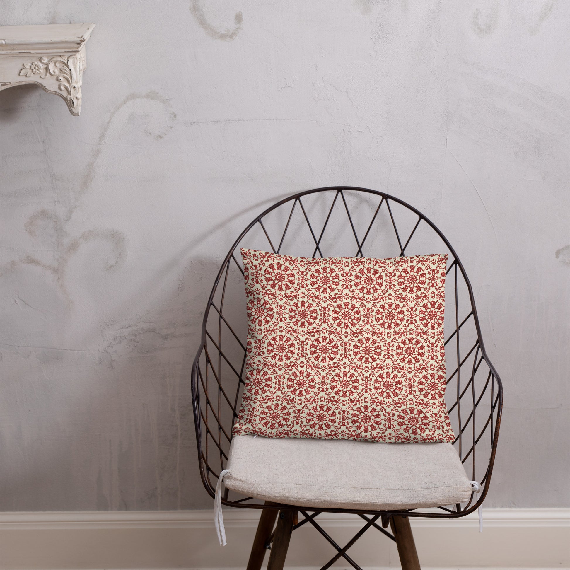 18″×18″ throw pillow with the ‘Decagon’ terracotta and beige geometric pattern on a wire chair against an ornate plaster wall.