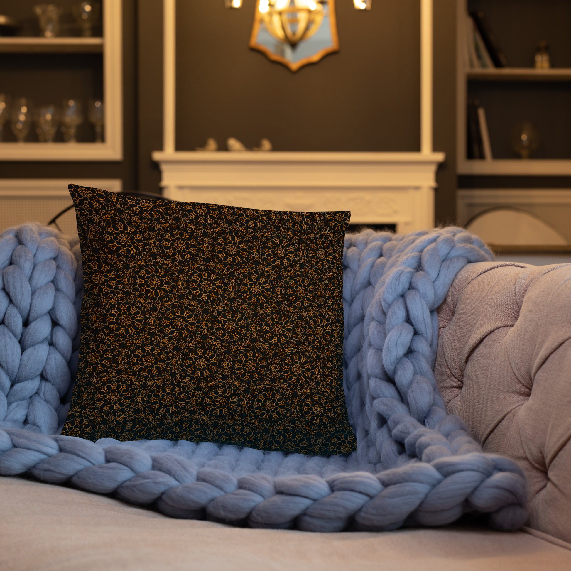 18″×18″ throw pillow with the 'Enneagon' black & gold geometric pattern on a sofa with chunky knit blanket.
