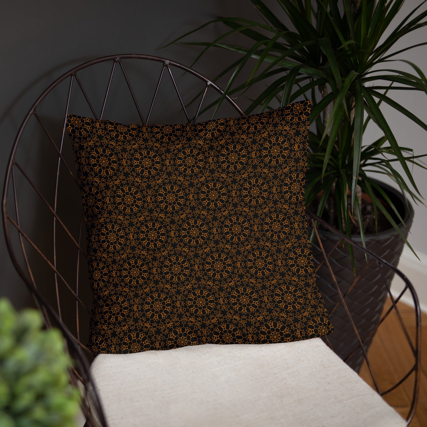18″×18″ throw pillow with the 'Enneagon' black & gold geometric pattern on a wire chair.