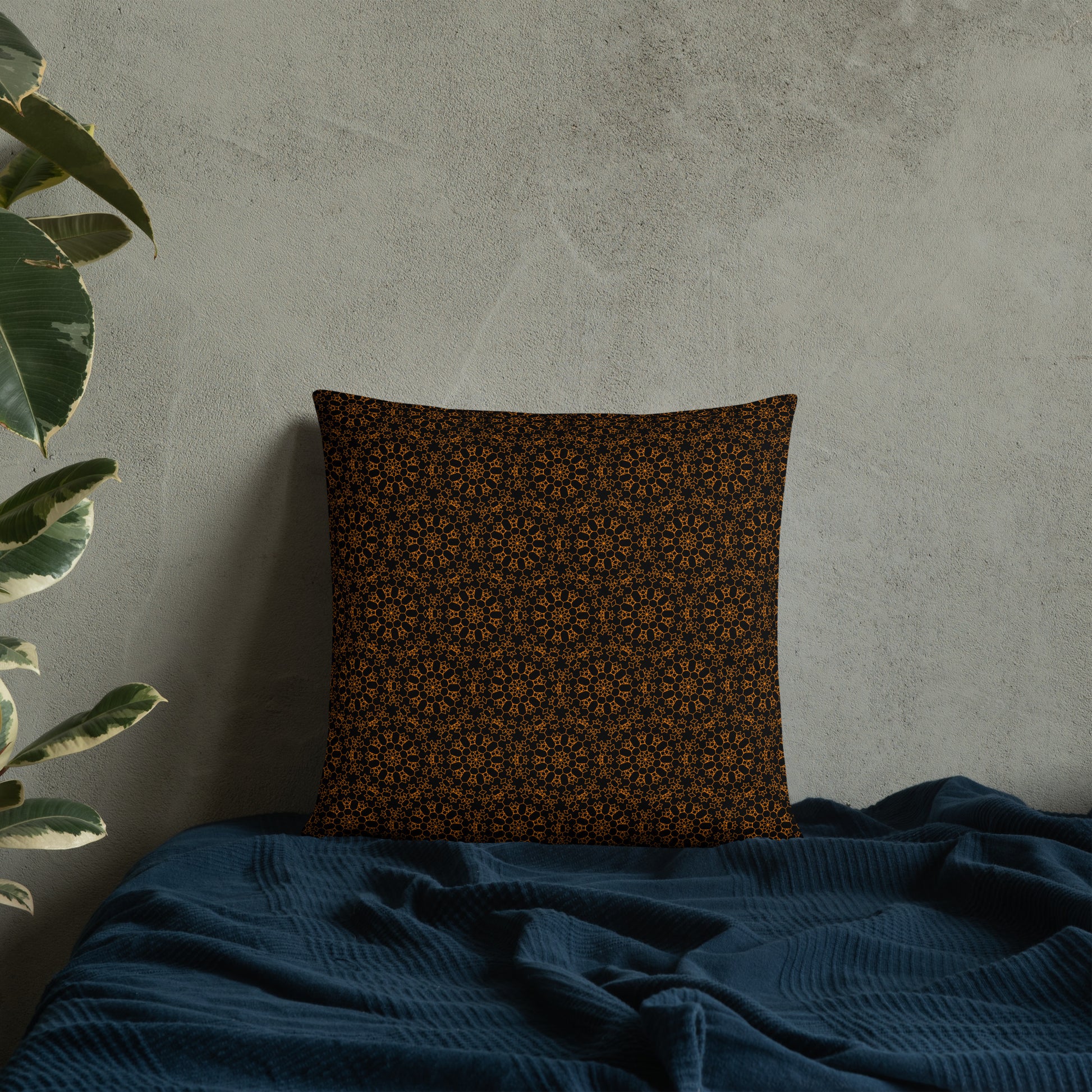 18″×18″ throw pillow with the 'Enneagon' black & gold geometric pattern on a bed with dark teal blanket.