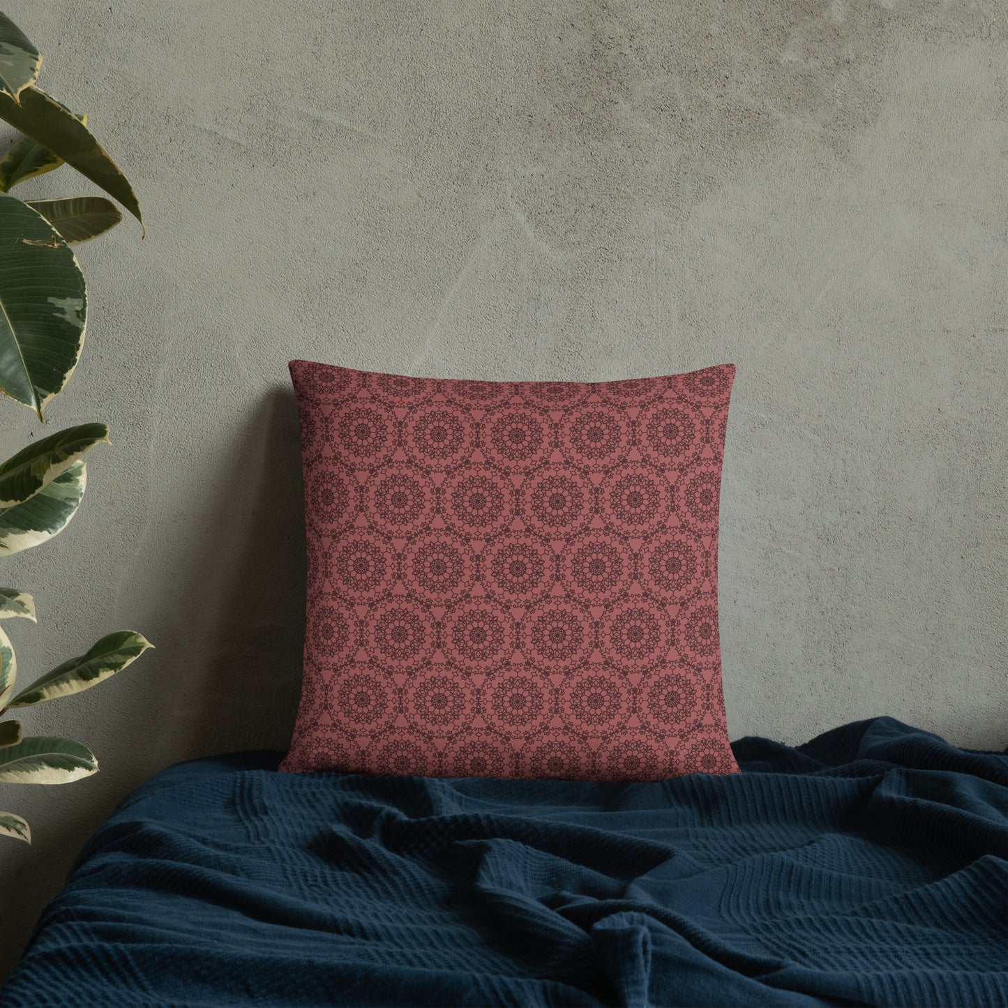 18″×18″ throw pillow with the 'Dodecagon' rose geometric pattern on bed with dark teal blanket against concrete wall.