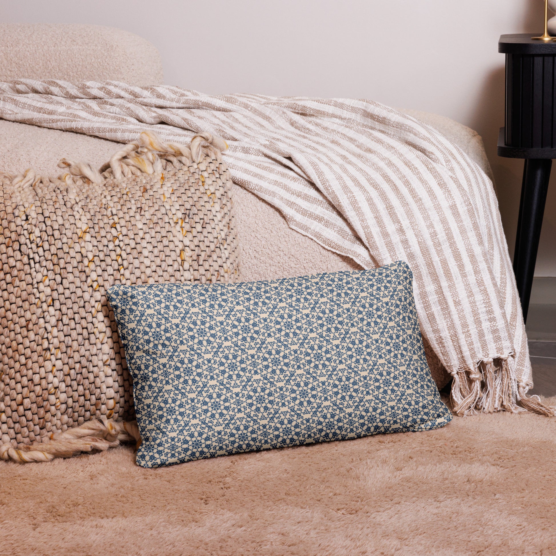 20″×12″ throw pillow with the ‘Octagon’ navy and beige geometric pattern on a bed with striped blanket.