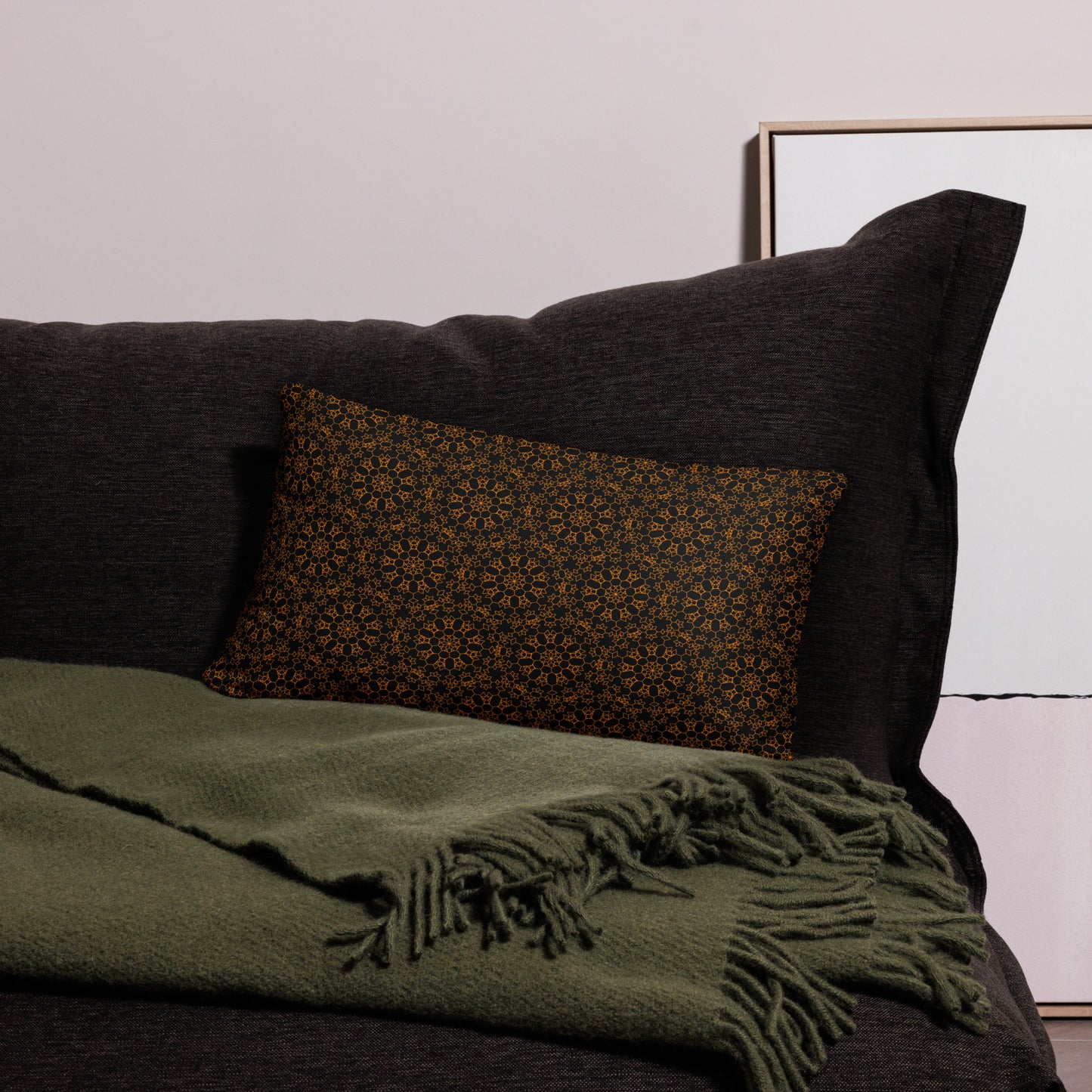 20″×12″ throw pillow with the 'Enneagon' black & gold geometric pattern on a dark sofa with green throw blanket.