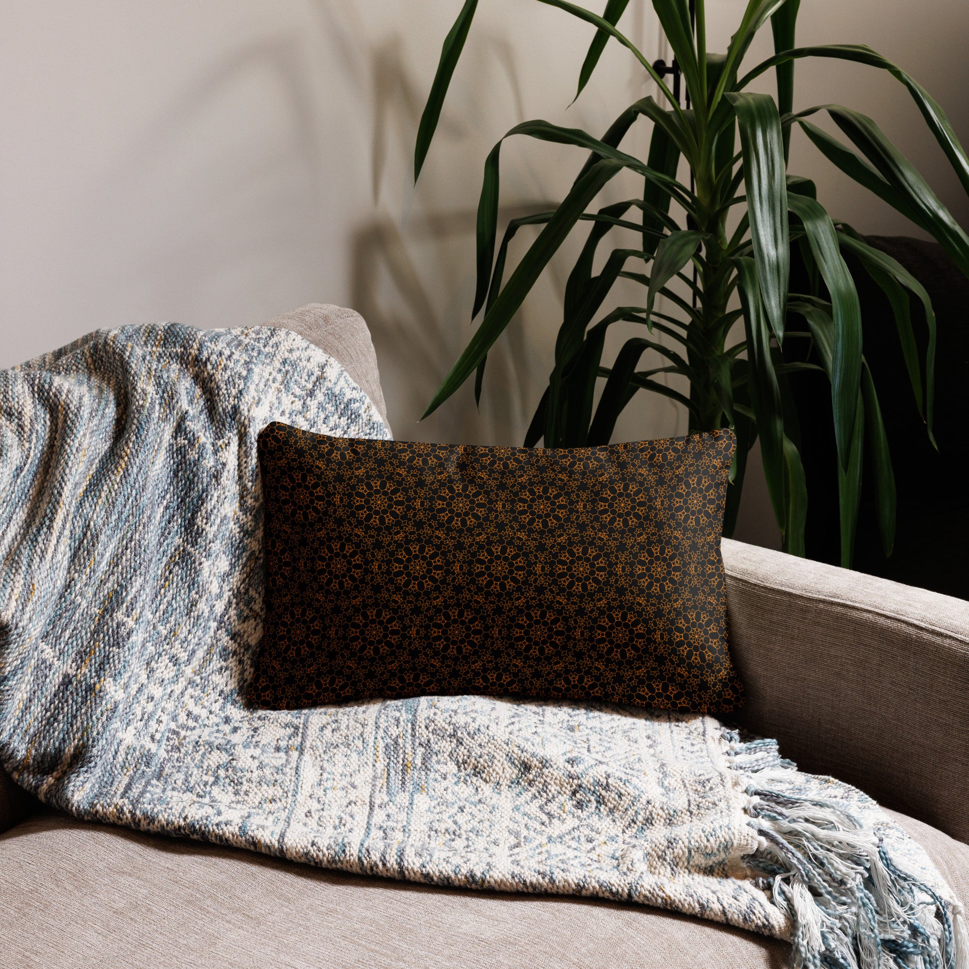 20″×12″ throw pillow with the 'Enneagon' black & gold geometric pattern on a sofa with textured throw blanket.