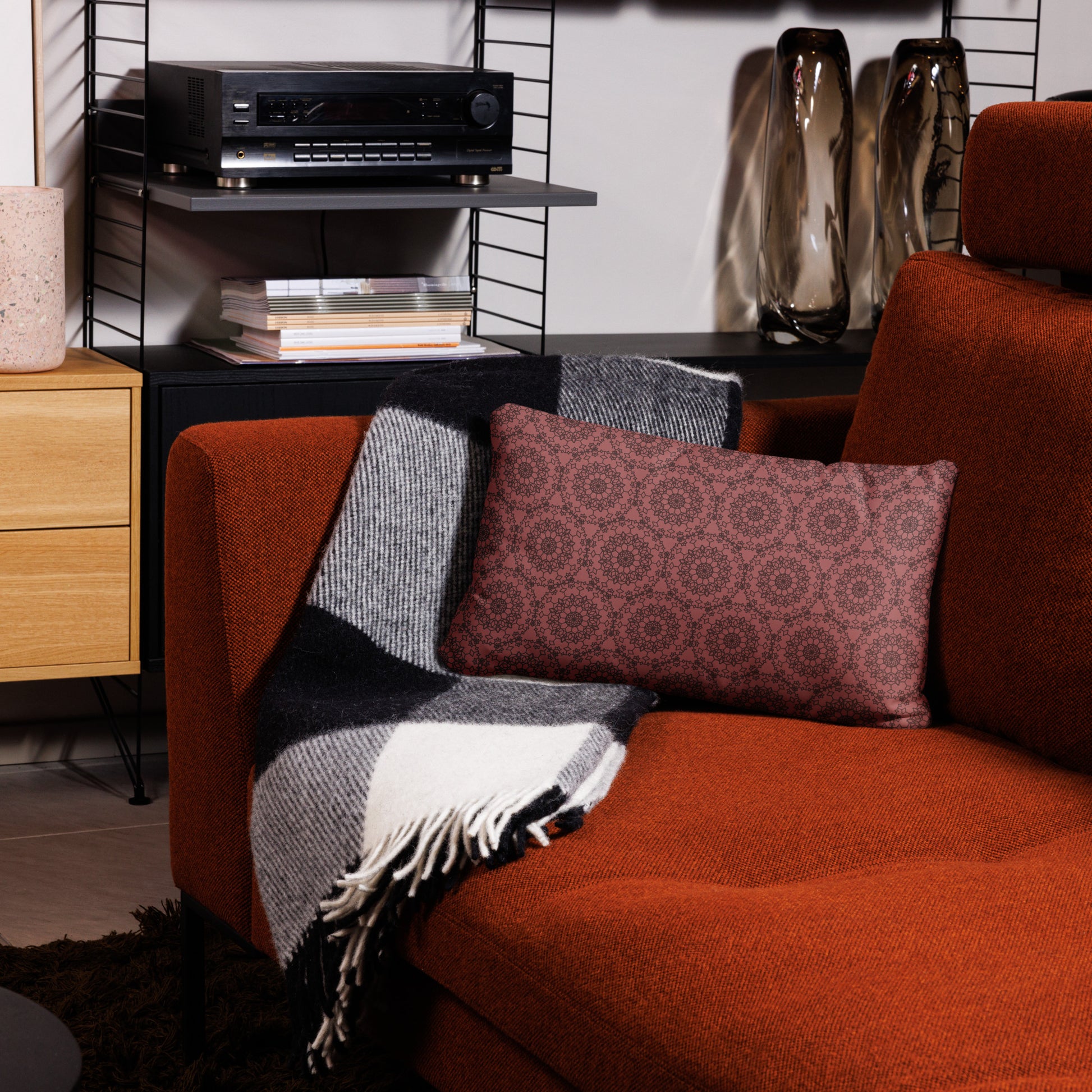 20″×12″ throw pillow with the 'Dodecagon' rose geometric pattern on orange armchair with checkered blanket.