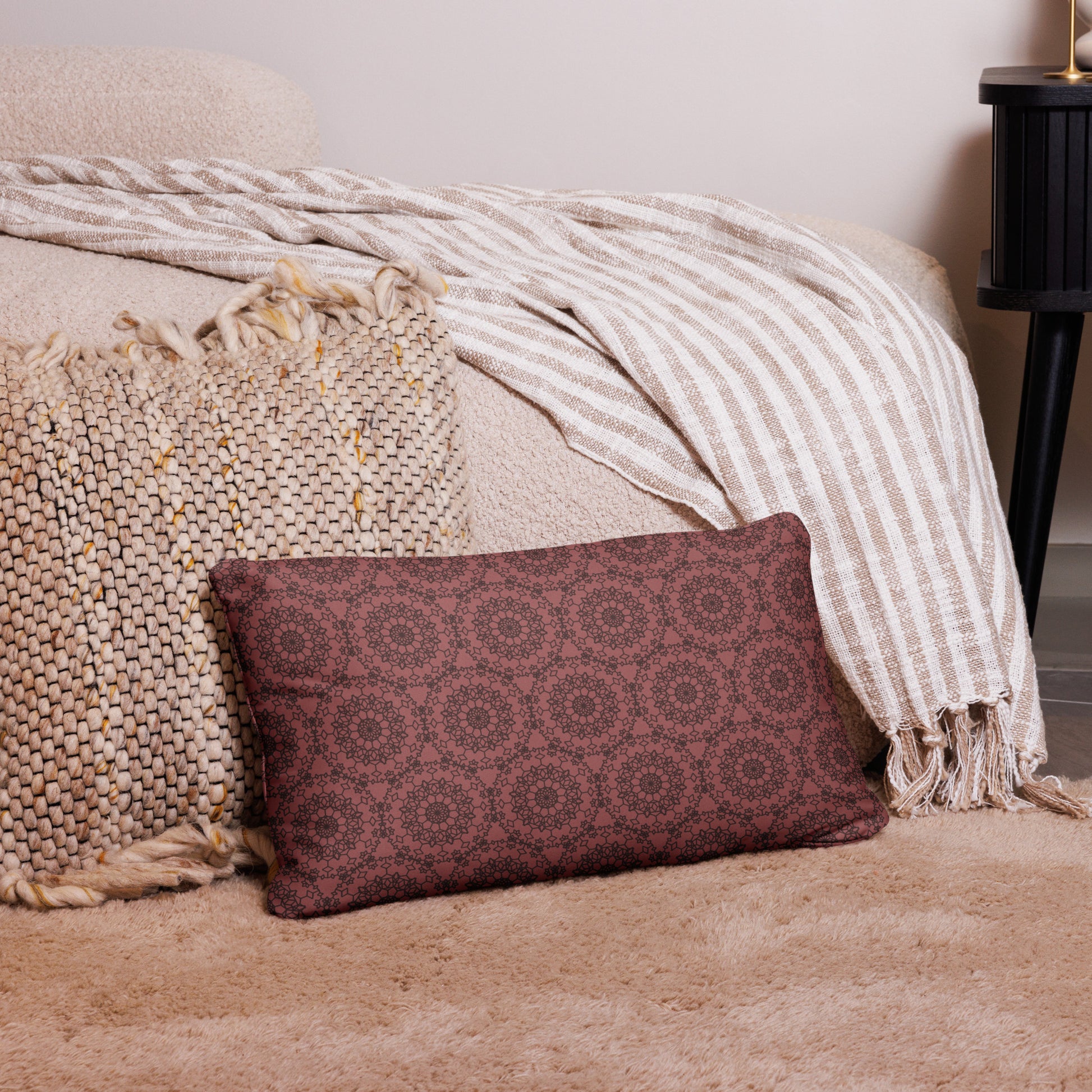 20″×12″ throw pillow with the 'Dodecagon' rose geometric pattern on carpet beside bed with striped throw.