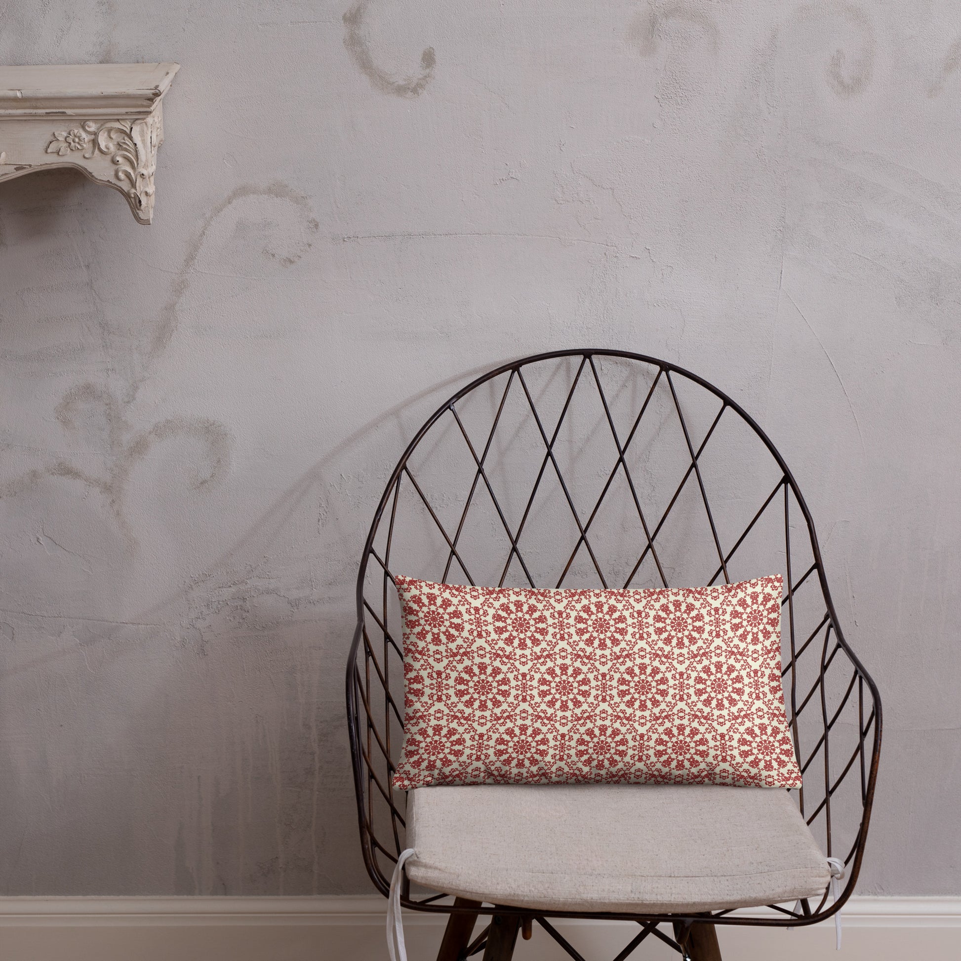 20″×12″ throw pillow with the ‘Decagon’ terracotta and beige geometric pattern on a wire chair against an ornate plaster wall.