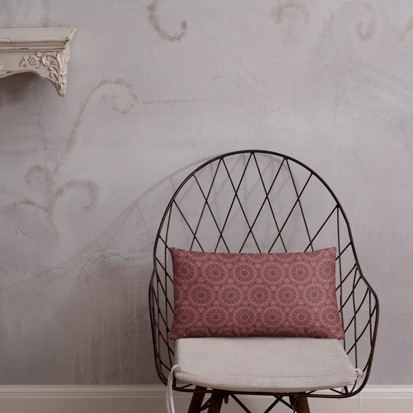 20″×12″ throw pillow with the 'Dodecagon' rose geometric pattern on wire chair with white cushion against textured wall.
