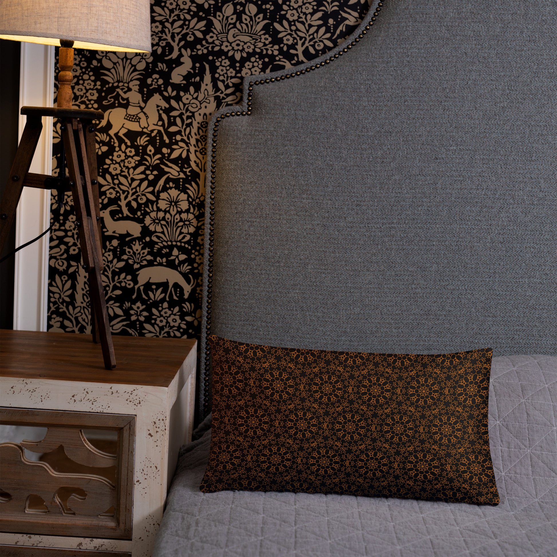 20″×12″ throw pillow with the 'Enneagon' black & gold geometric pattern on a bed with upholstered headboard.