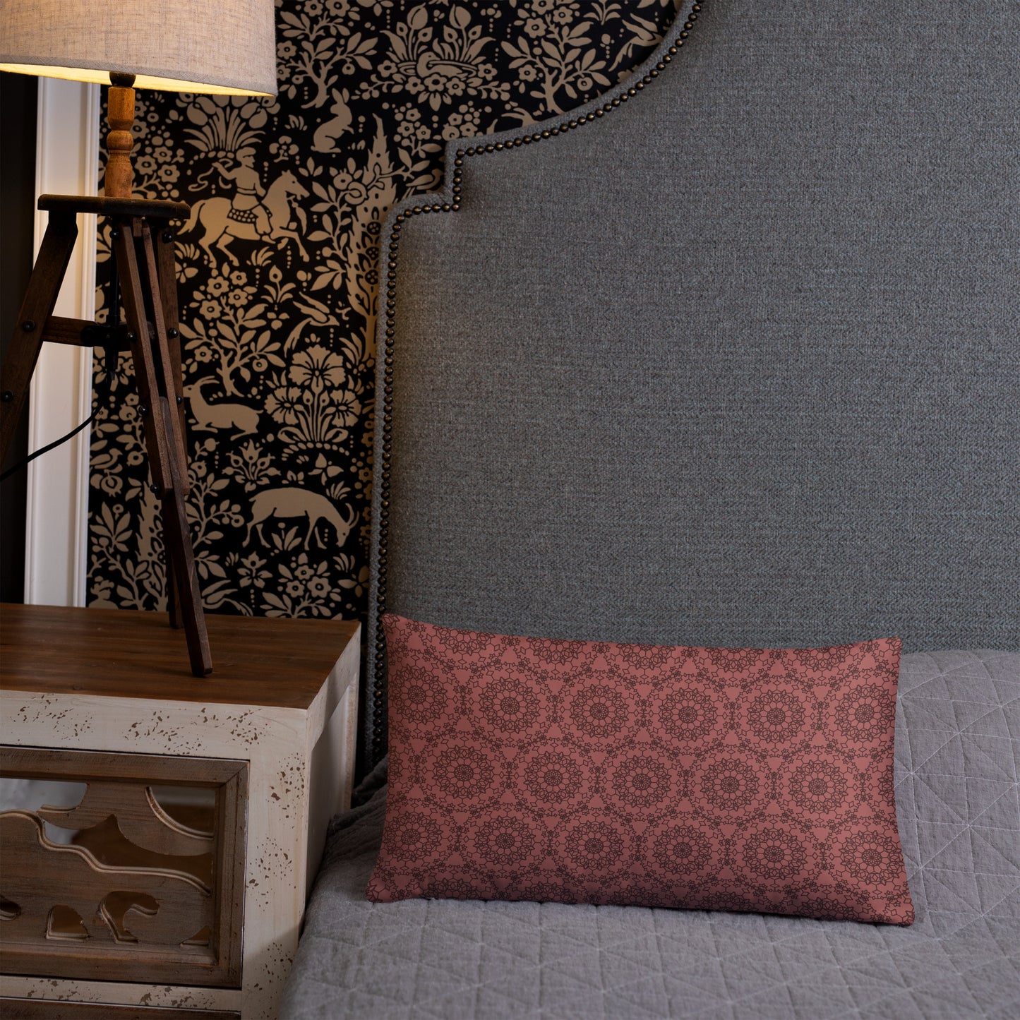 20″×12″ throw pillow with the 'Dodecagon' rose geometric pattern on bed beside grey upholstered headboard with lamp.