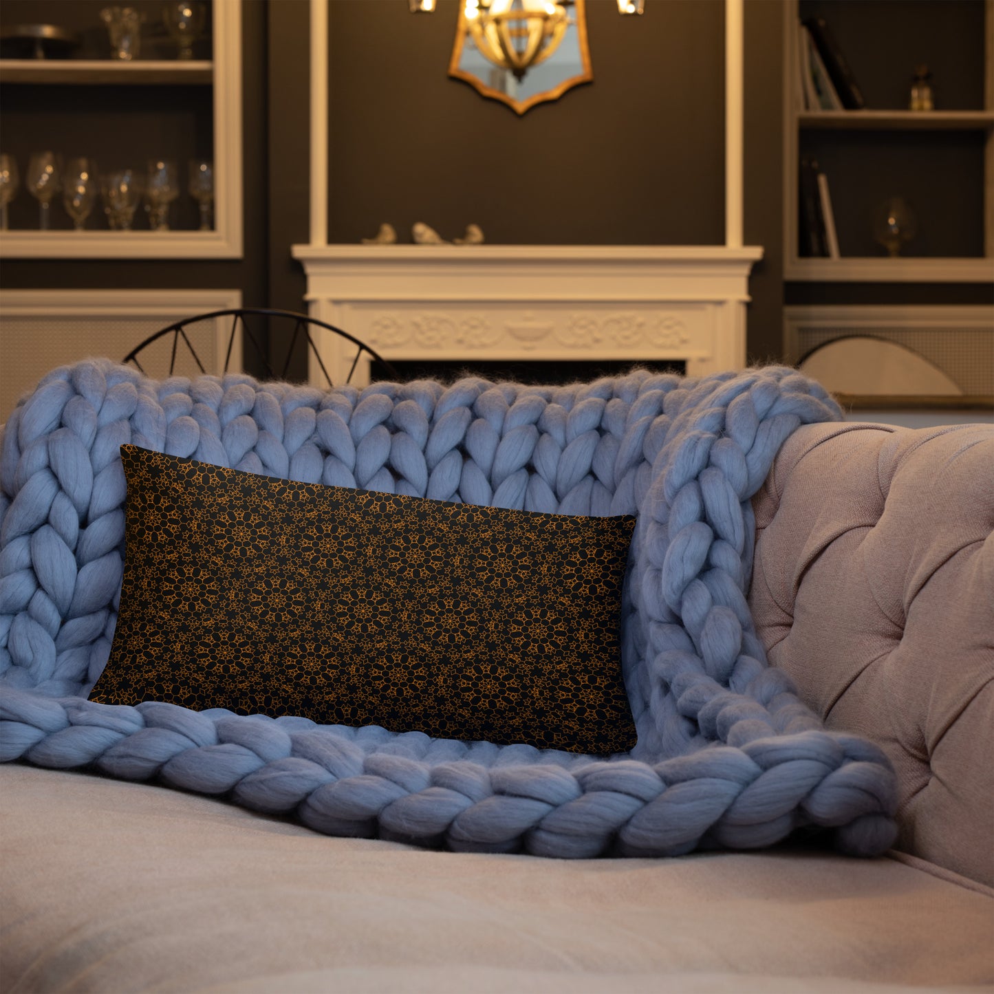 20″×12″ throw pillow with the 'Enneagon' black & gold geometric pattern on a sofa with chunky knit blanket.