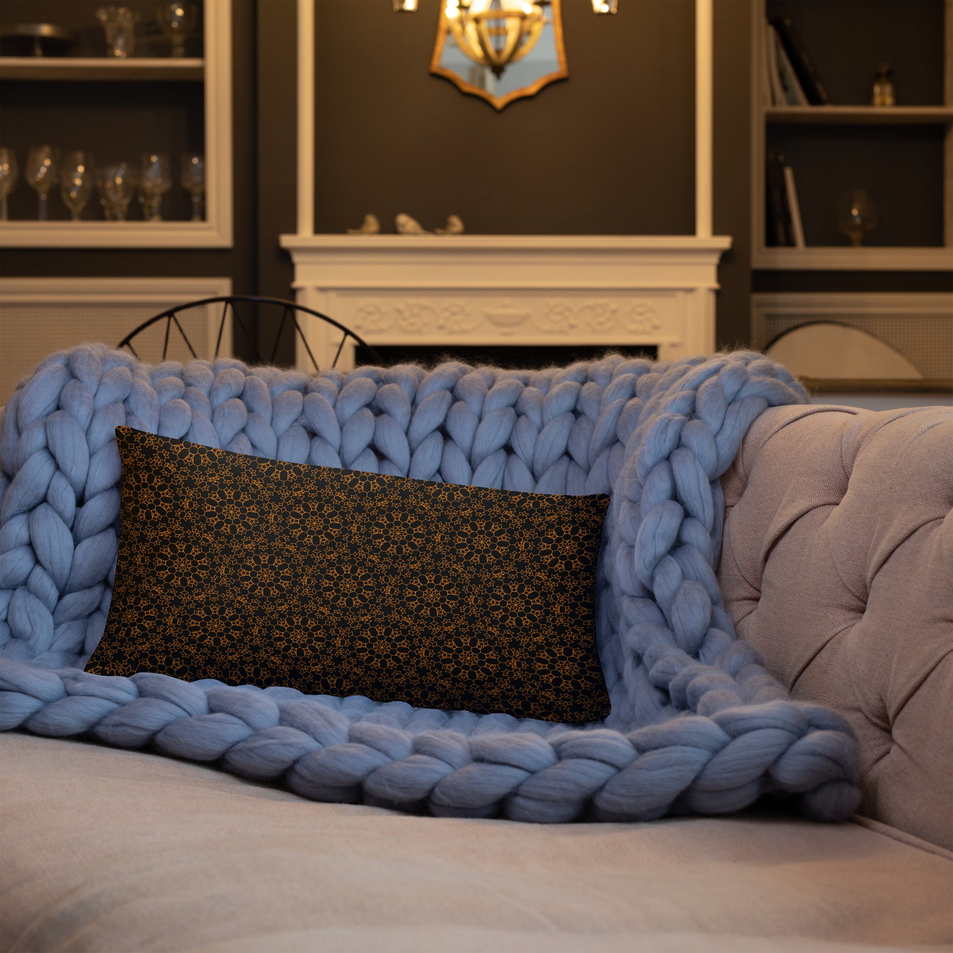 20″×12″ throw pillow with the 'Enneagon' black & gold geometric pattern on a sofa with chunky knit blanket.