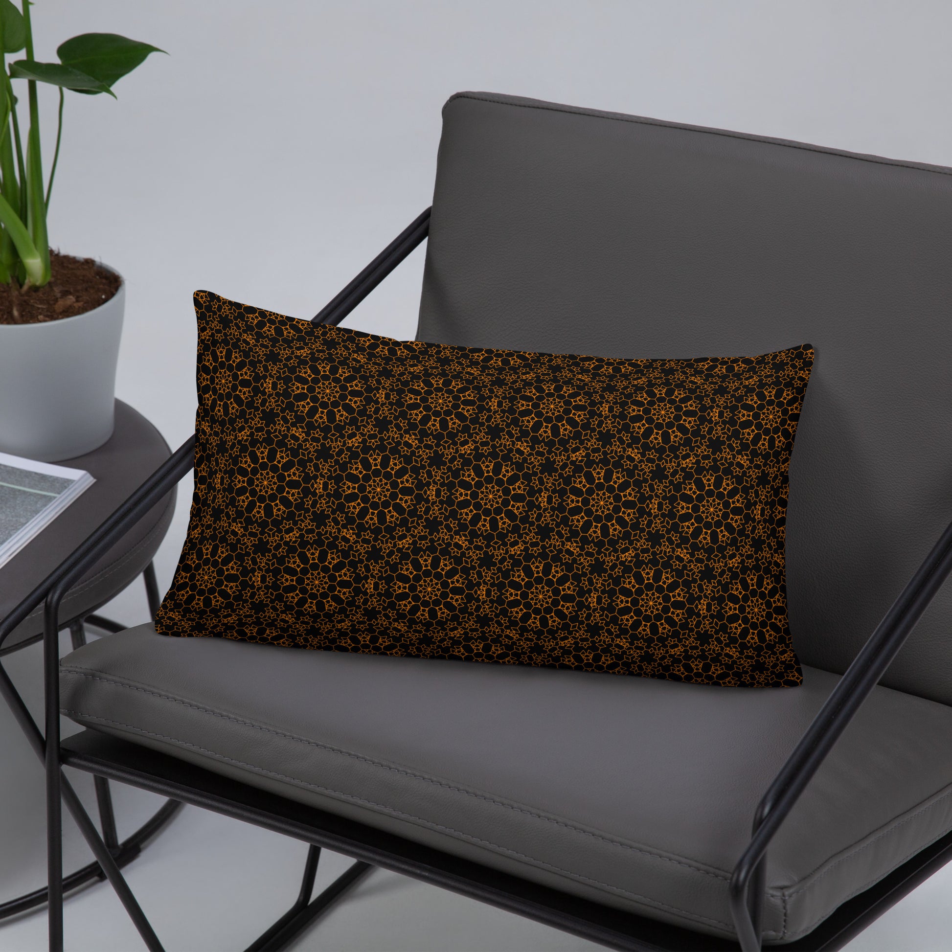 20″×12″ throw pillow with the 'Enneagon' black & gold geometric pattern on a wire chair.