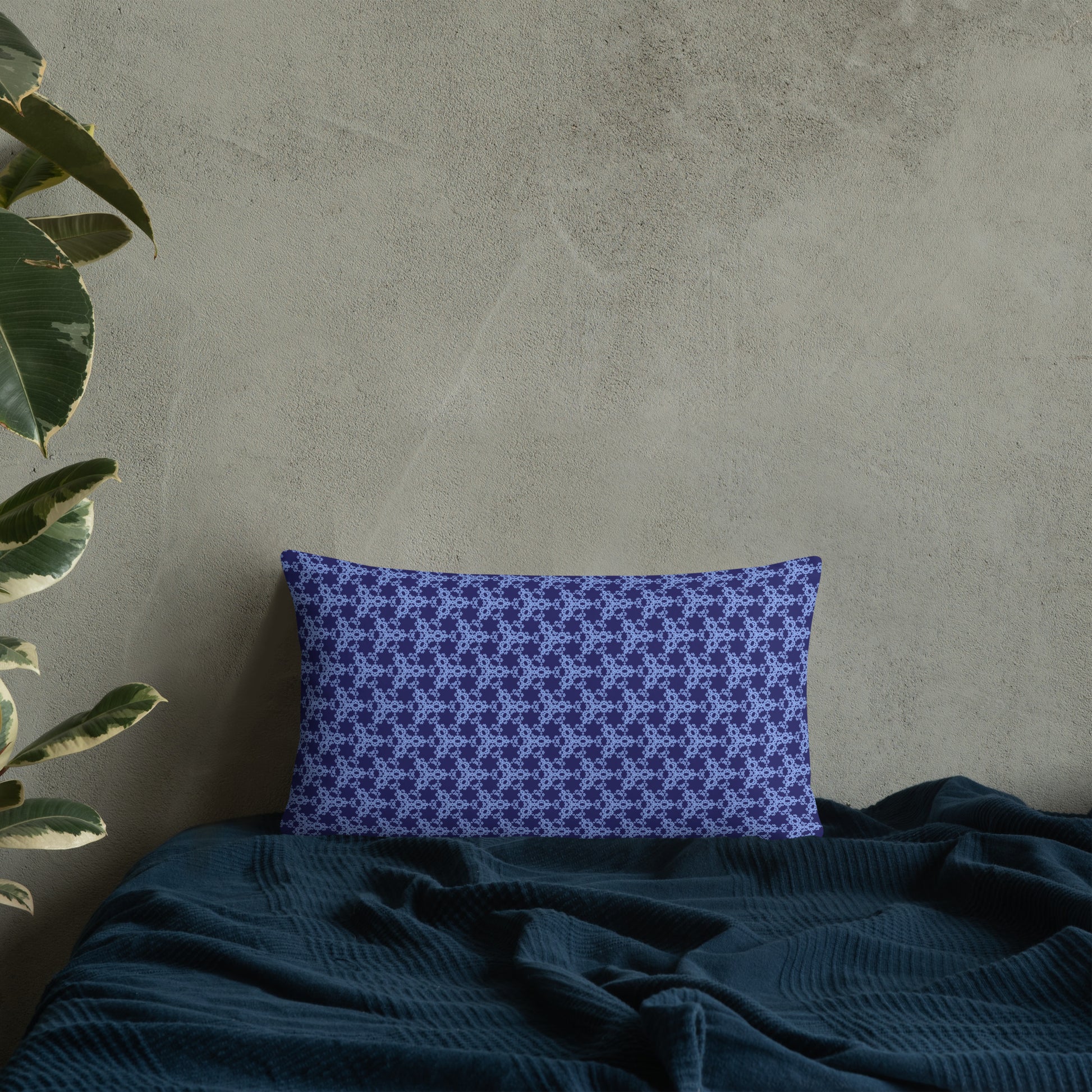20″×12″ throw pillow with the 'Trigon' navy and blue geometric pattern on a bed.