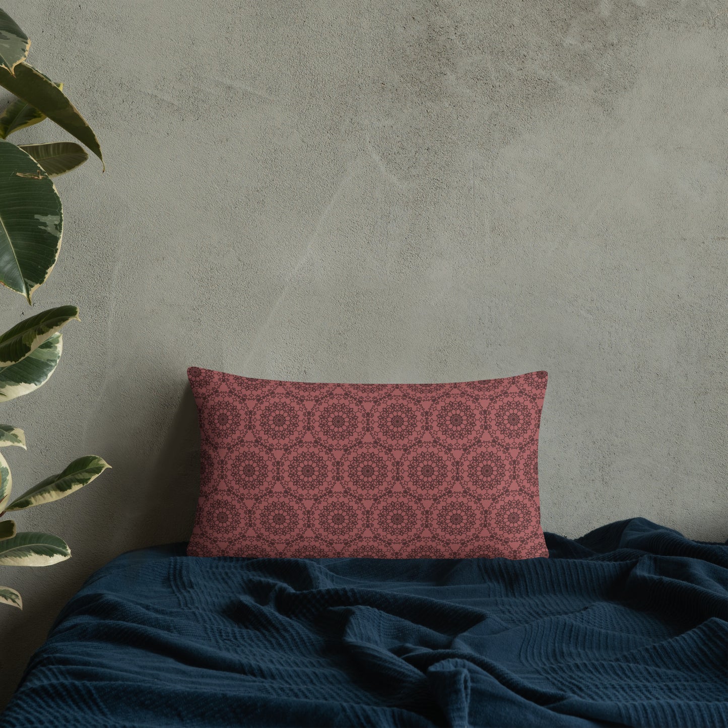 20″×12″ throw pillow with the 'Dodecagon' rose geometric pattern on bed with dark teal blanket against concrete wall.