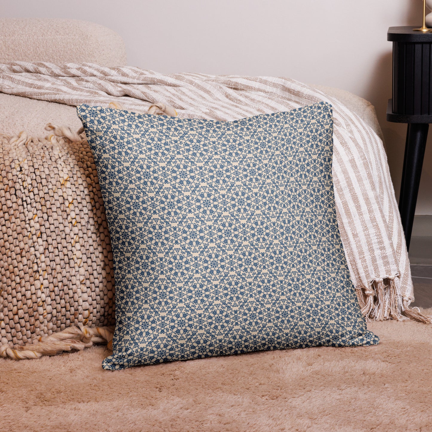 22″×22″ throw pillow with the ‘Octagon’ navy and beige geometric pattern on a bed with striped blanket.