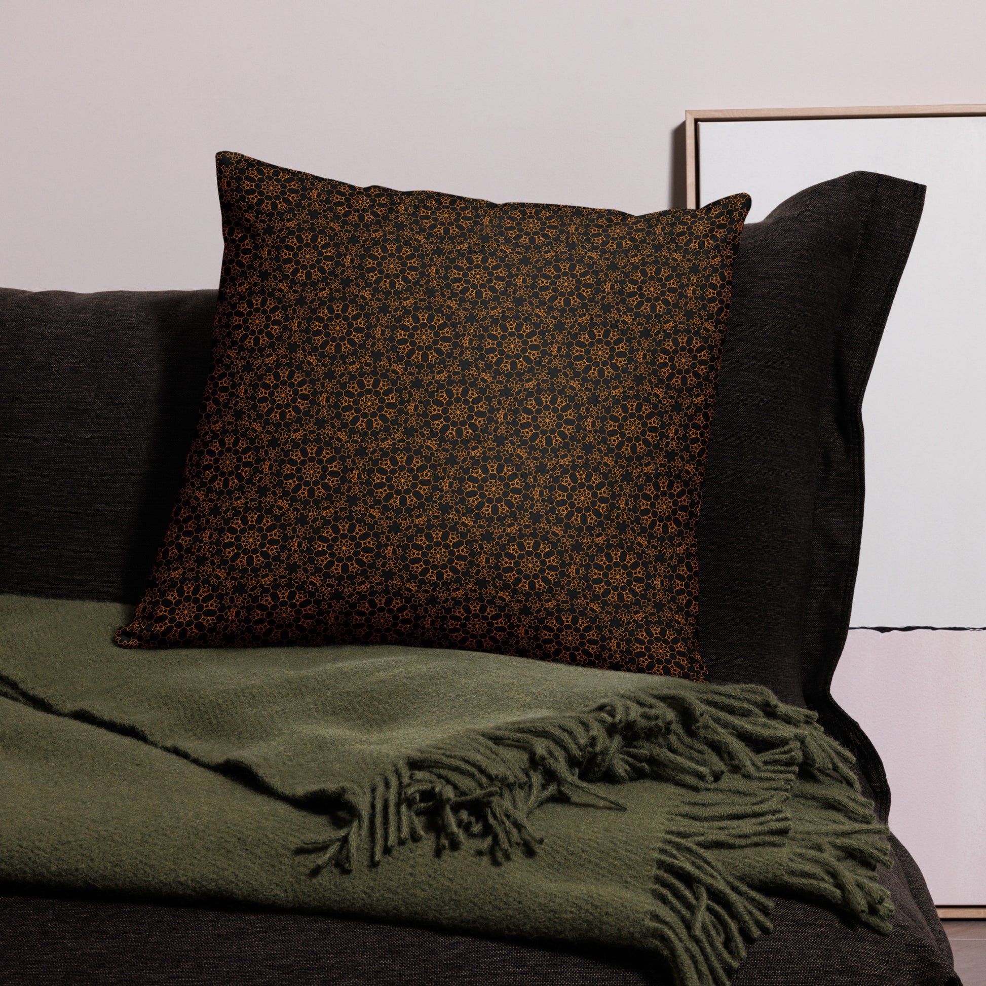 22″×22″ throw pillow with the 'Enneagon' black & gold geometric pattern on a dark sofa with green throw blanket.