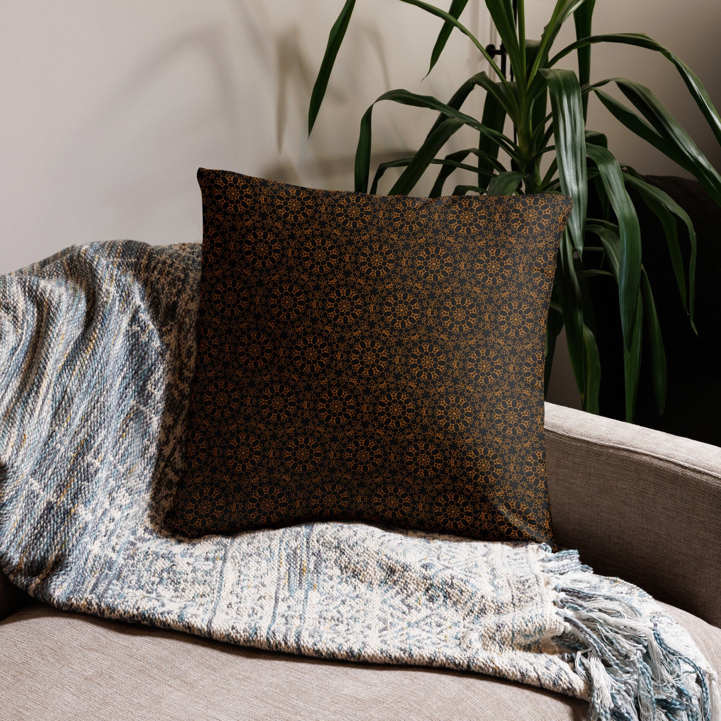 22″×22″ throw pillow with the 'Enneagon' black & gold geometric pattern on a sofa with textured throw blanket.