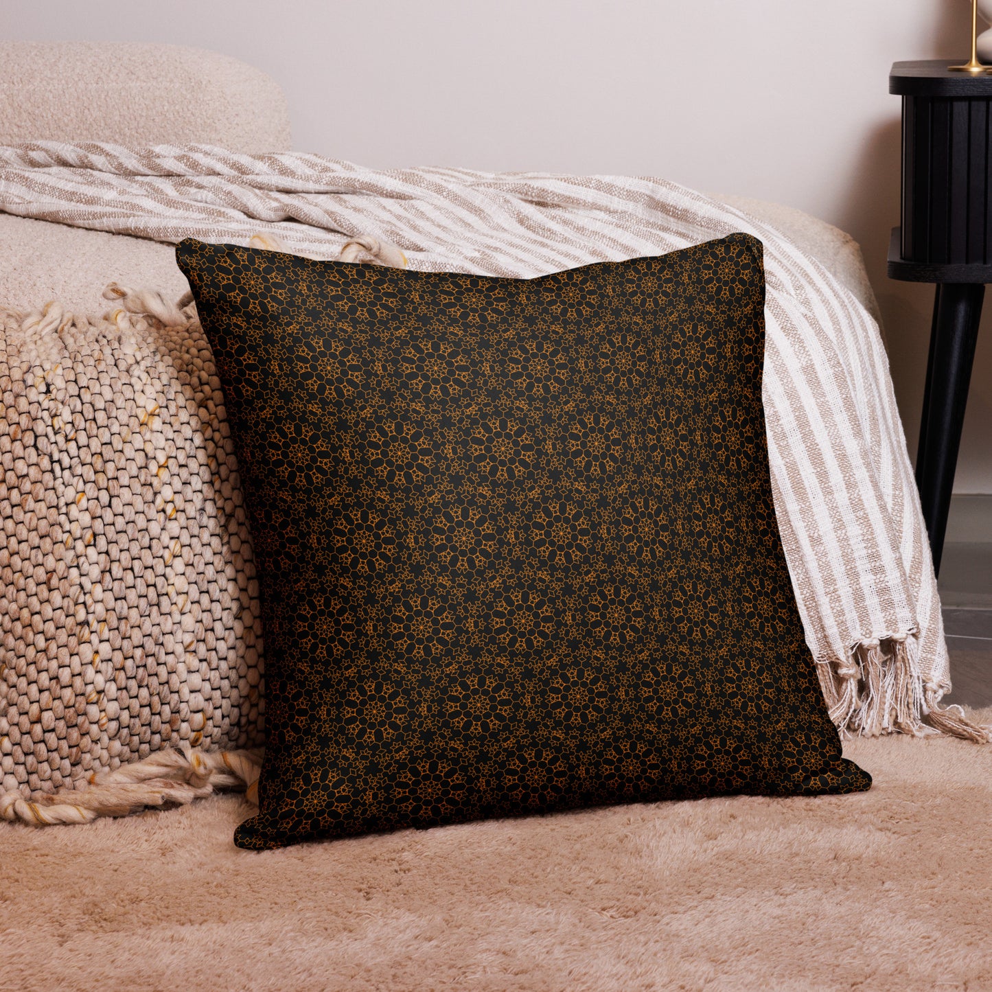 22″×22″ throw pillow with the 'Enneagon' black & gold geometric pattern on a bed with striped blanket.