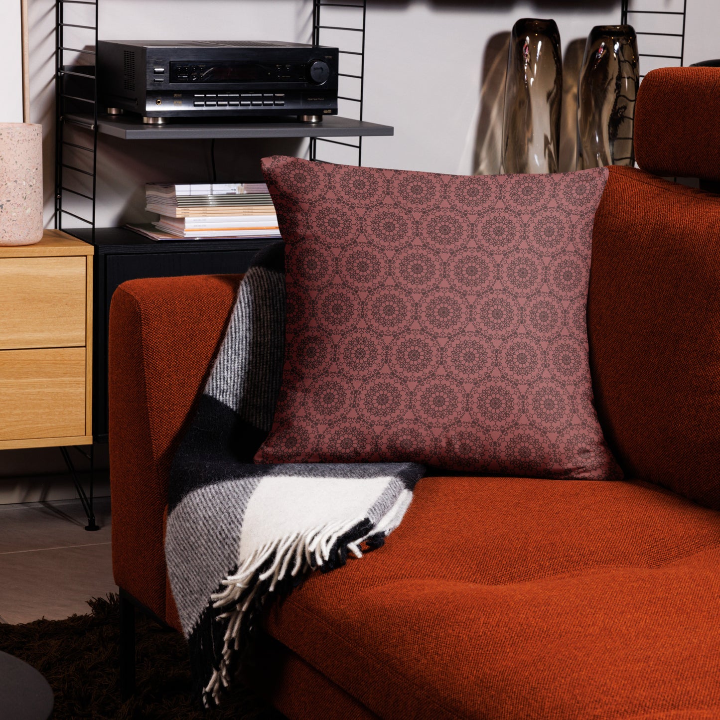 22″×22″ throw pillow with the 'Dodecagon' rose geometric pattern on orange armchair with checkered blanket.