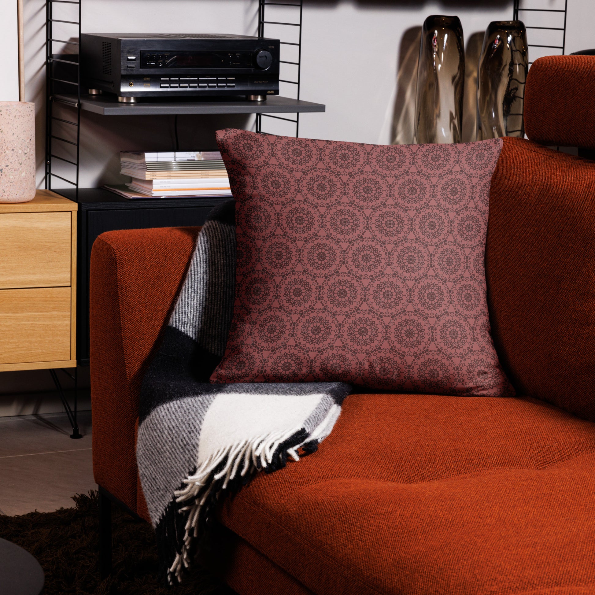 22″×22″ throw pillow with the 'Dodecagon' rose geometric pattern on orange armchair with checkered blanket.