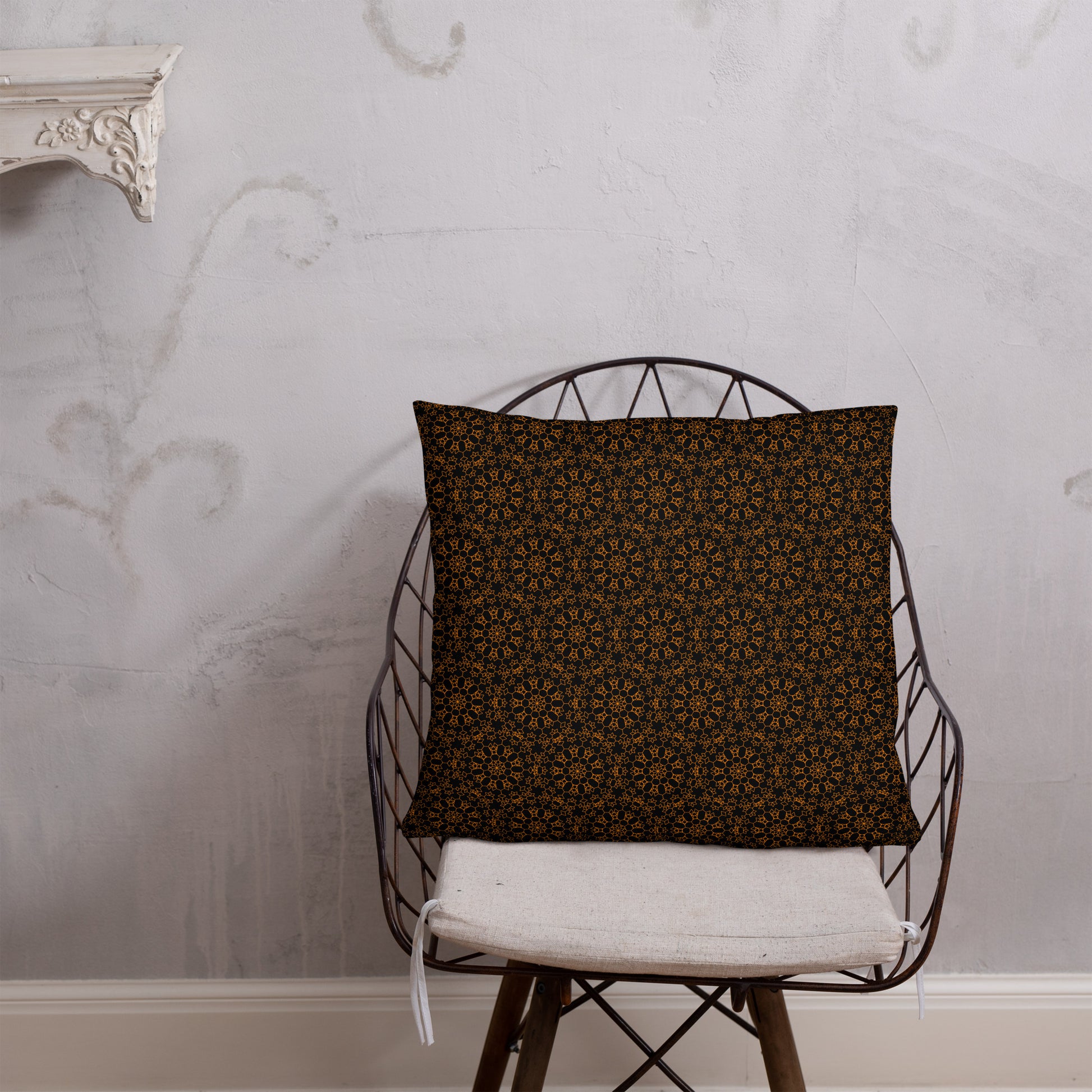 22″×22″ throw pillow with the 'Enneagon' black & gold geometric pattern on a wire chair.