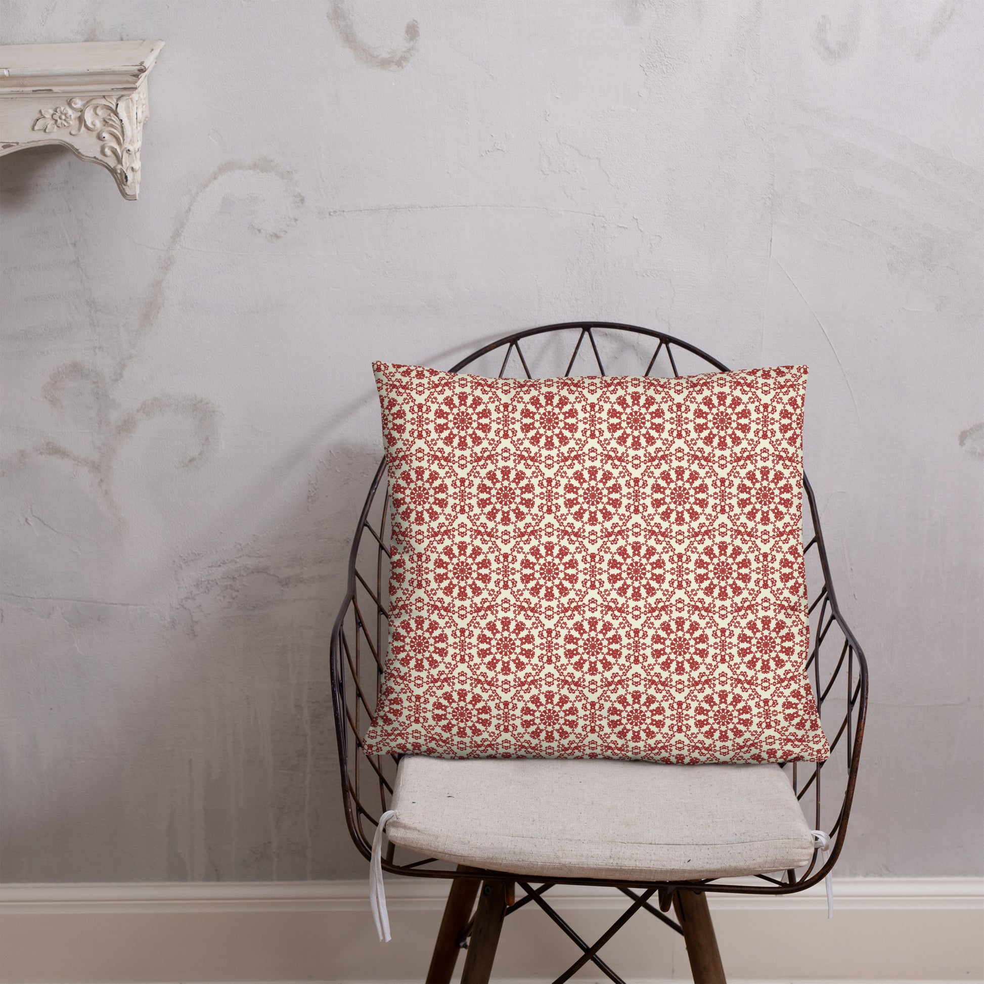 22″×22″ throw pillow with the ‘Decagon’ terracotta and beige geometric pattern on a wire chair against an ornate plaster wall.
