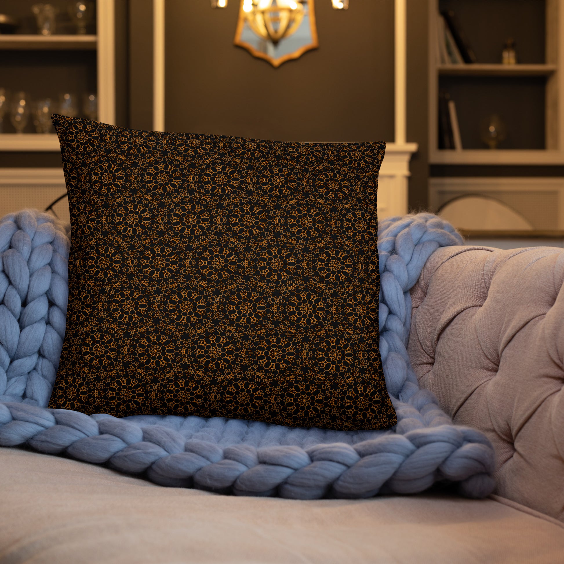 22″×22″ throw pillow with the 'Enneagon' black & gold geometric pattern on a sofa with chunky knit blanket.