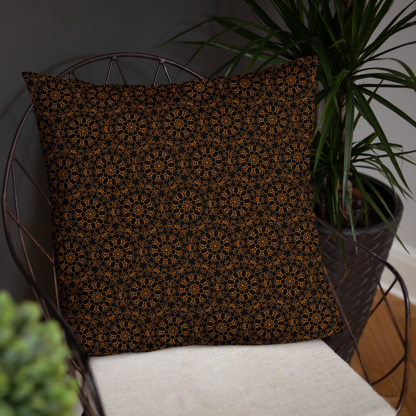 22″×22″ throw pillow with the 'Enneagon' black & gold geometric pattern on a wire chair.