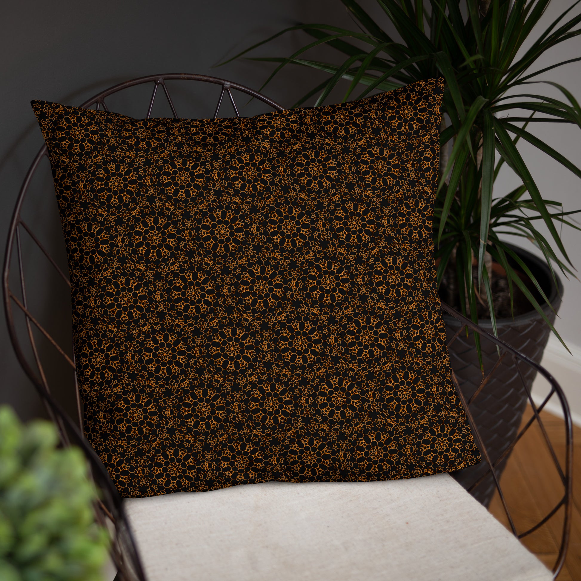 22″×22″ throw pillow with the 'Enneagon' black & gold geometric pattern on a wire chair.