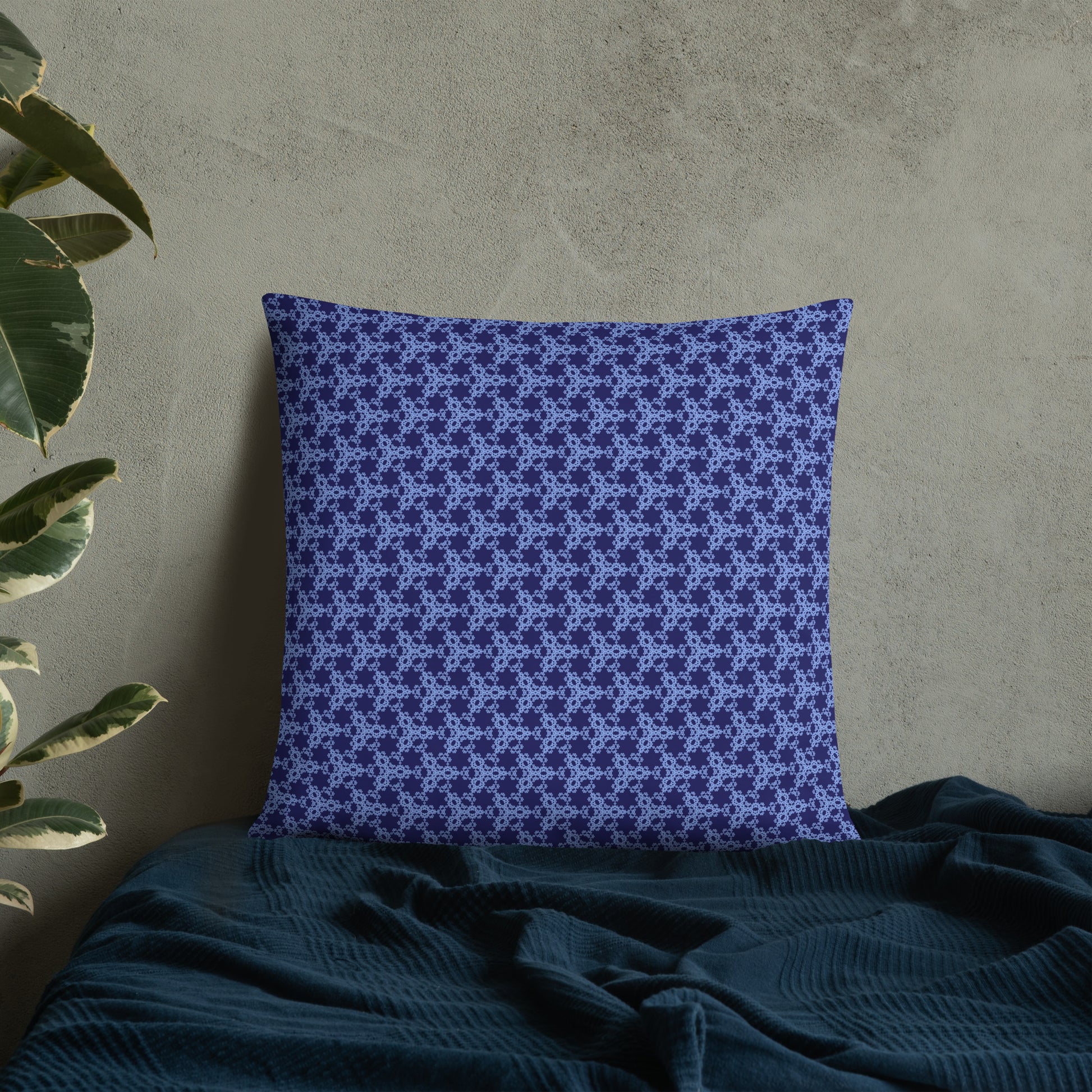 22″×22″ throw pillow with the 'Trigon' navy and blue geometric pattern on a bed.