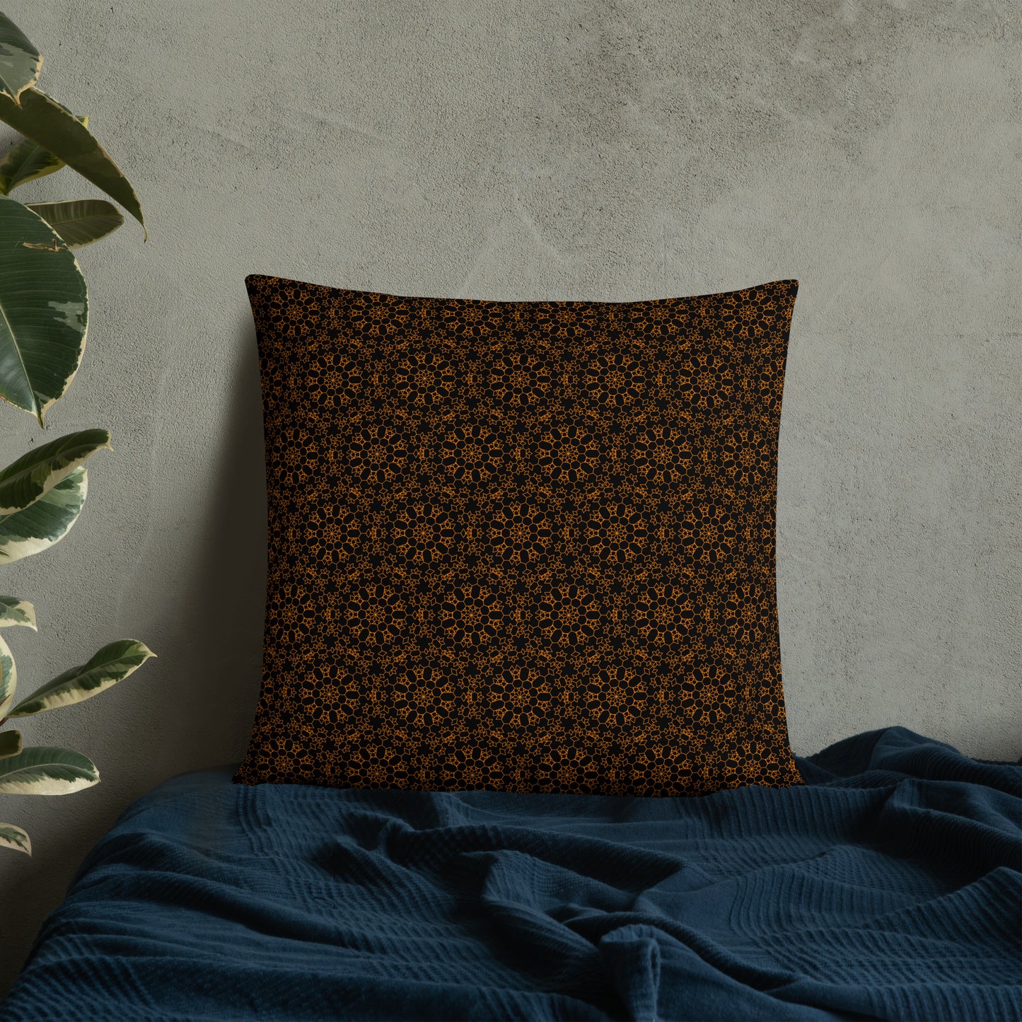 22″×22″ throw pillow with the 'Enneagon' black & gold geometric pattern on a bed with dark teal blanket.