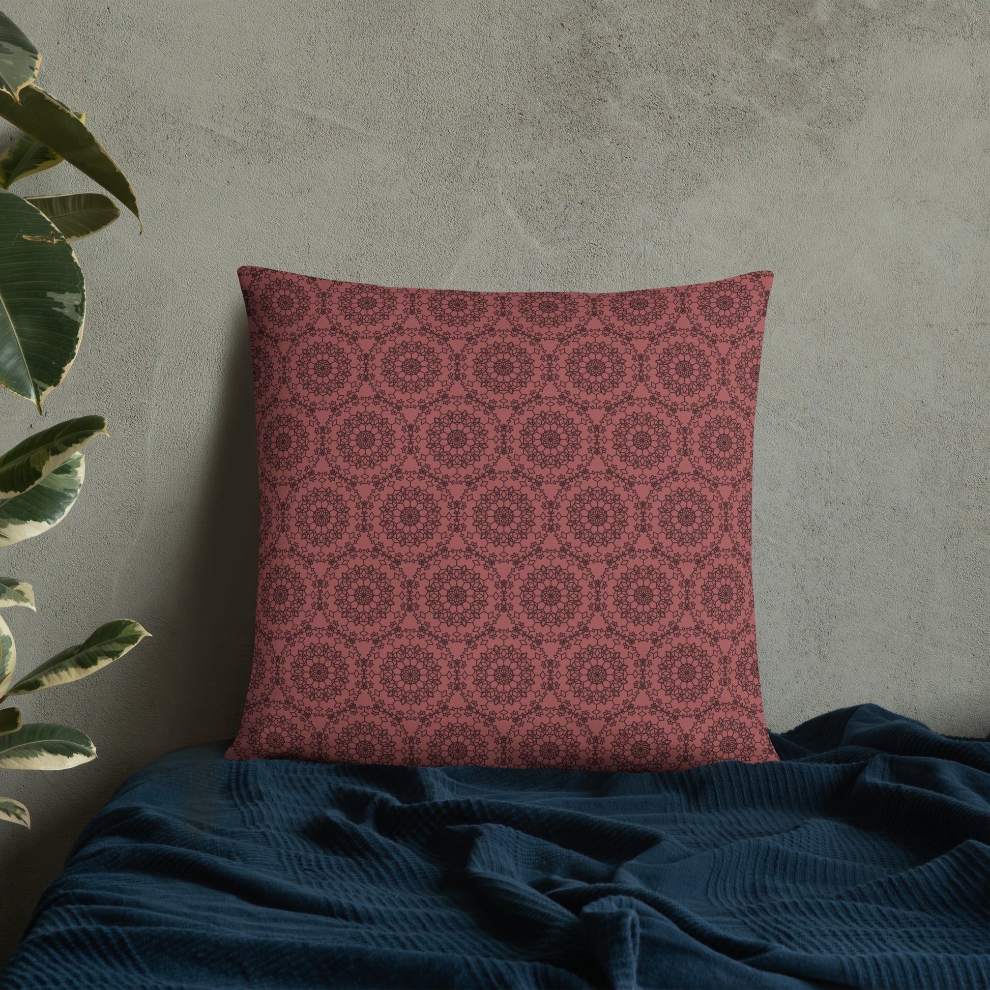 22″×22″ throw pillow with the 'Dodecagon' rose geometric pattern on bed with dark teal blanket against concrete wall.