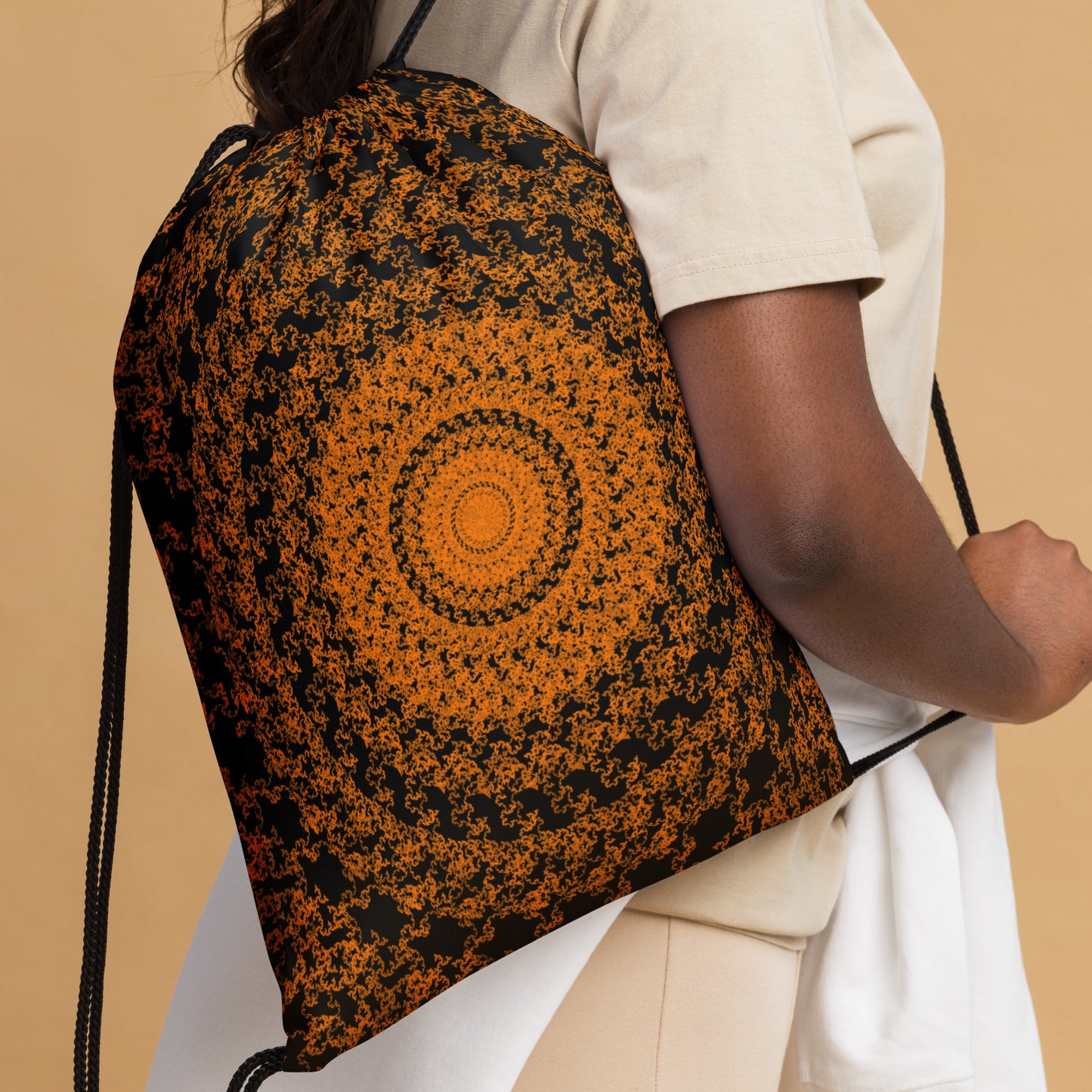 Close up of the drawstring bag with the 'The Sun' black and orange fractal design slung over a woman's shoulder.