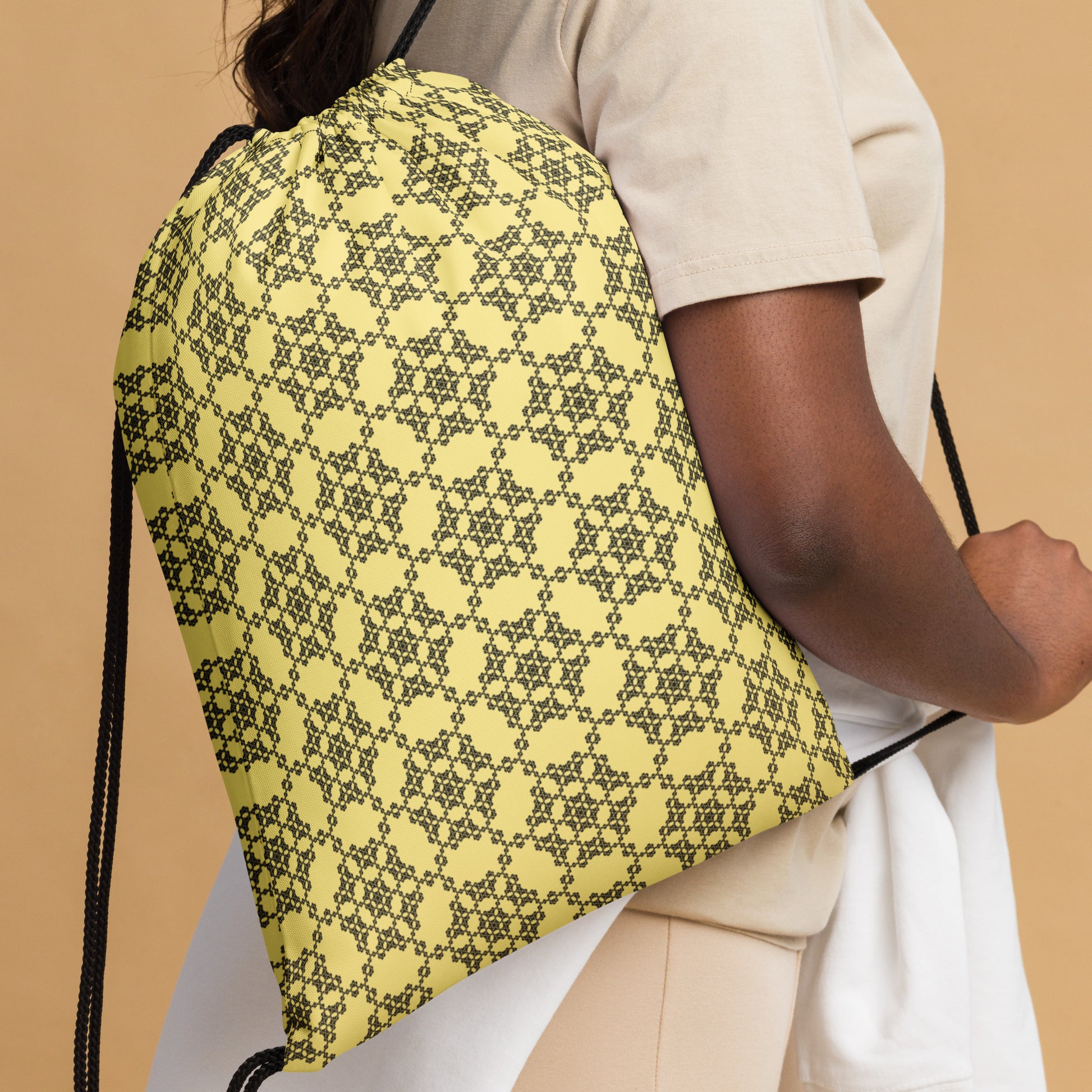 Close up of the drawstring bag with the 'Hexagon' yellow and black fractal geometric pattern slung over a woman's shoulder.