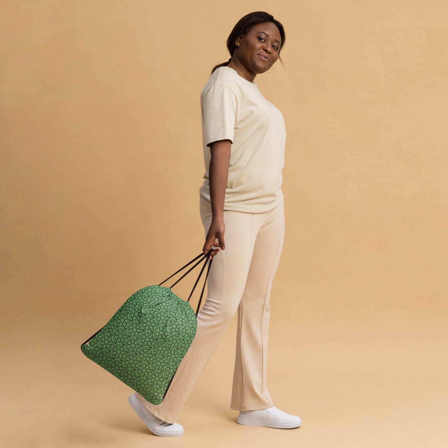 Woman slinging the drawstring bag with the 'Heptagon' green fractal geometric pattern.