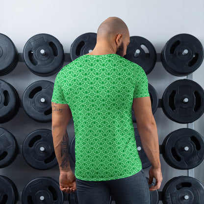 Back shot of an athletic man standing in front of a gym weight plate rack wearing the t-shirt with the 'Tetragon' green fractal geometric pattern.