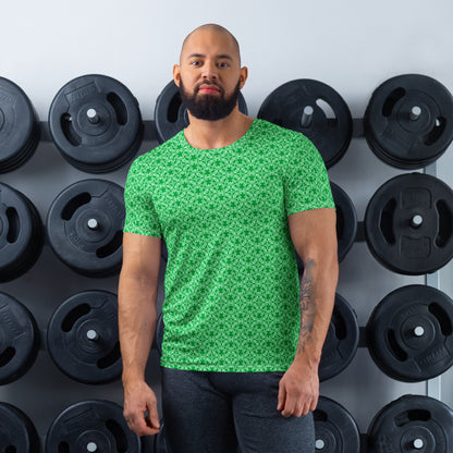 Athletic man standing in front of a gym weight plate rack wearing the t-shirt with the 'Tetragon' green fractal geometric pattern.