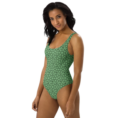 Left front shot of a model wearing the one-piece swimsuit with the 'Heptagon' green fractal geometric pattern.