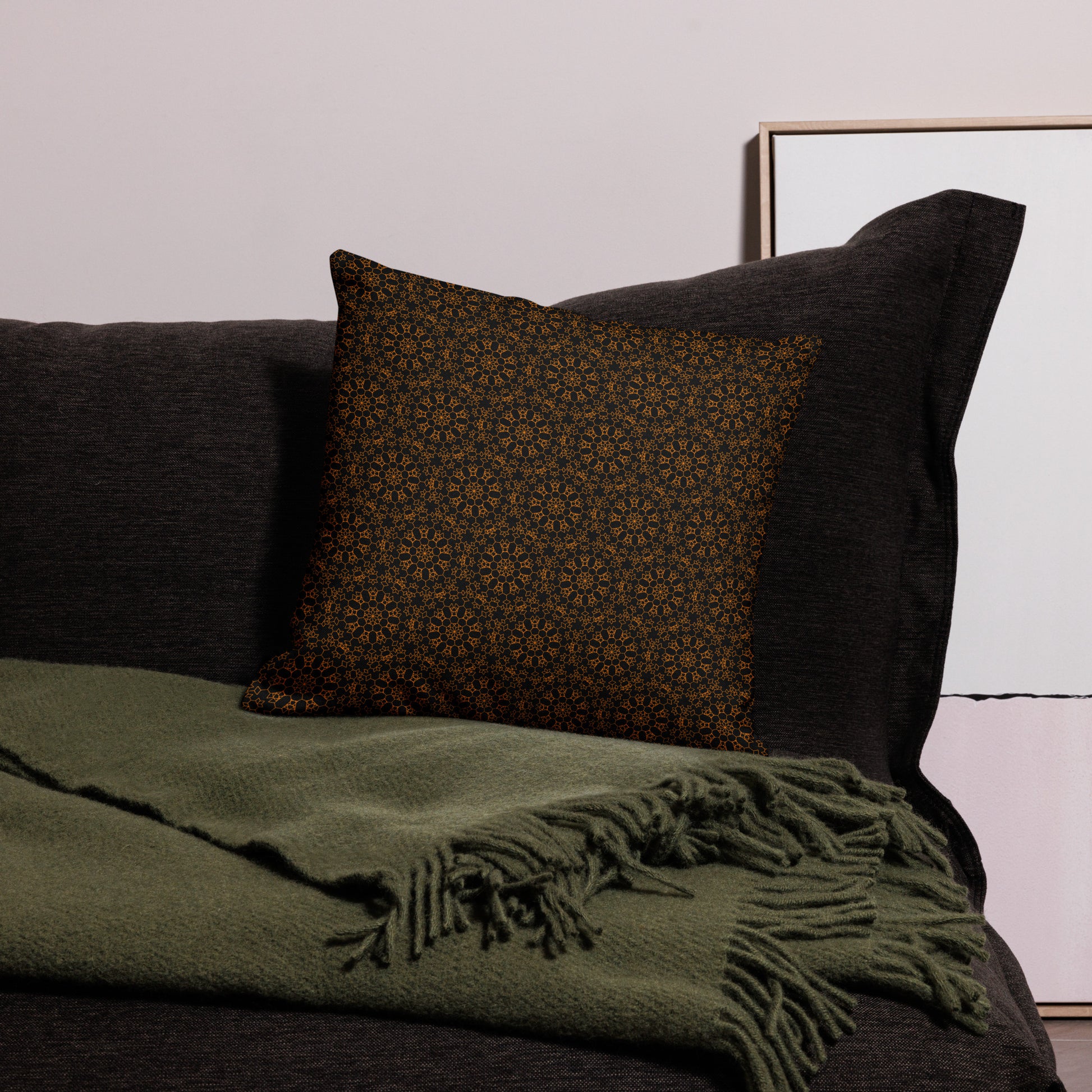 18″×18″ premium throw pillow with the 'Enneagon' black & gold geometric pattern on a dark sofa with green throw blanket.