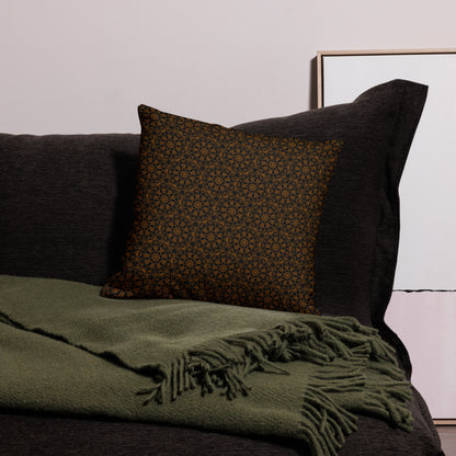 18″×18″ premium throw pillow with the 'Enneagon' black & gold geometric pattern on a dark sofa with green throw blanket.