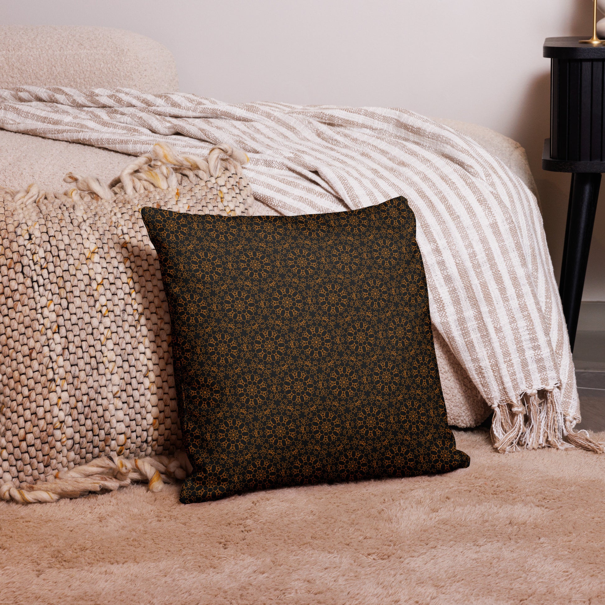 18″×18″ premium throw pillow with the 'Enneagon' black & gold geometric pattern on a bed with striped blanket.