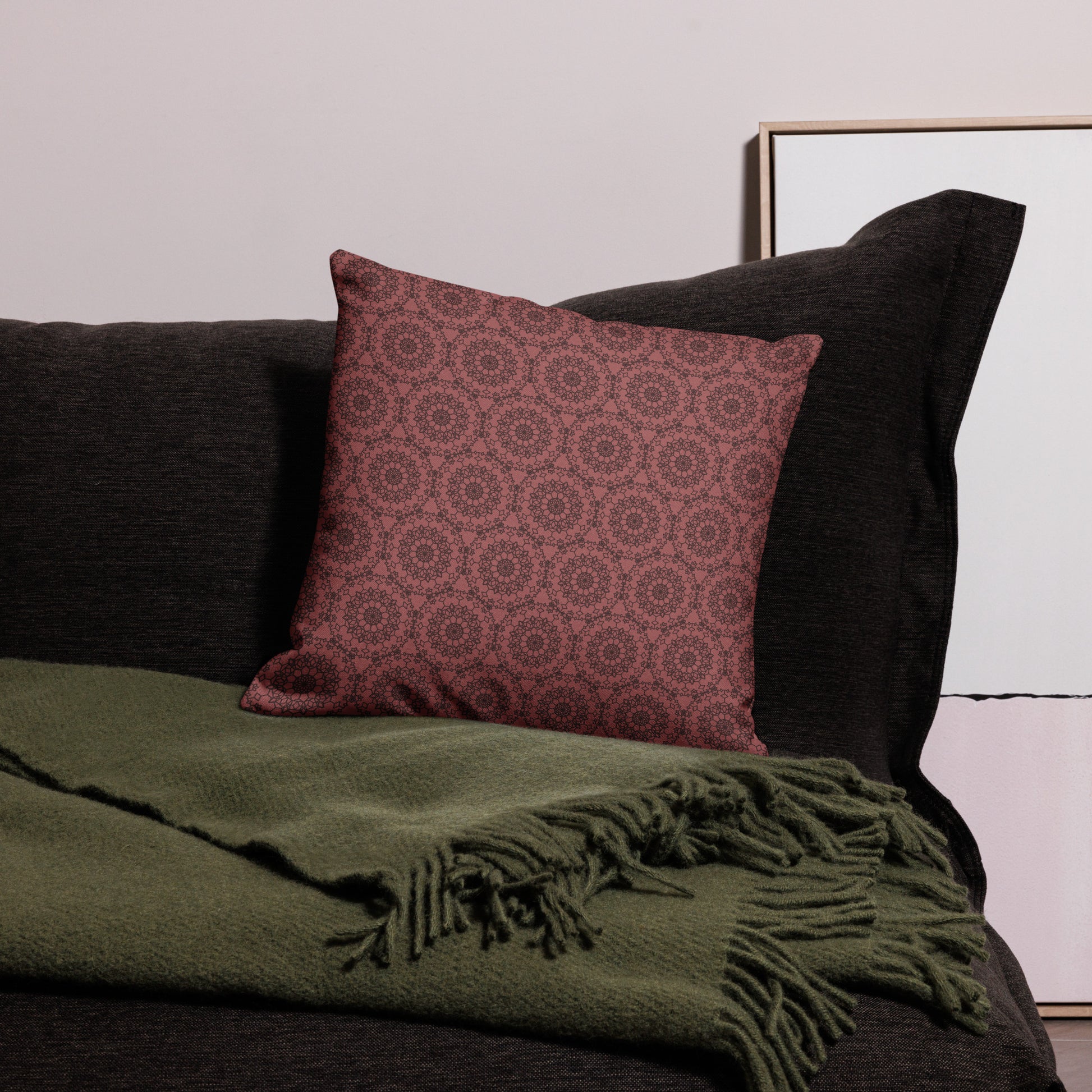 18″×18″ premium throw pillow with the 'Dodecagon' rose geometric pattern on dark sofa with green fringed throw.