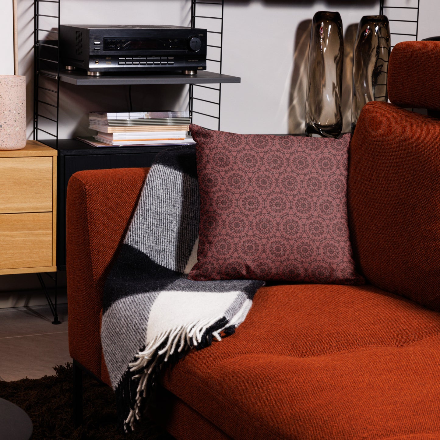 18″×18″ premium throw pillow with the 'Dodecagon' rose geometric pattern on orange armchair with checkered blanket.